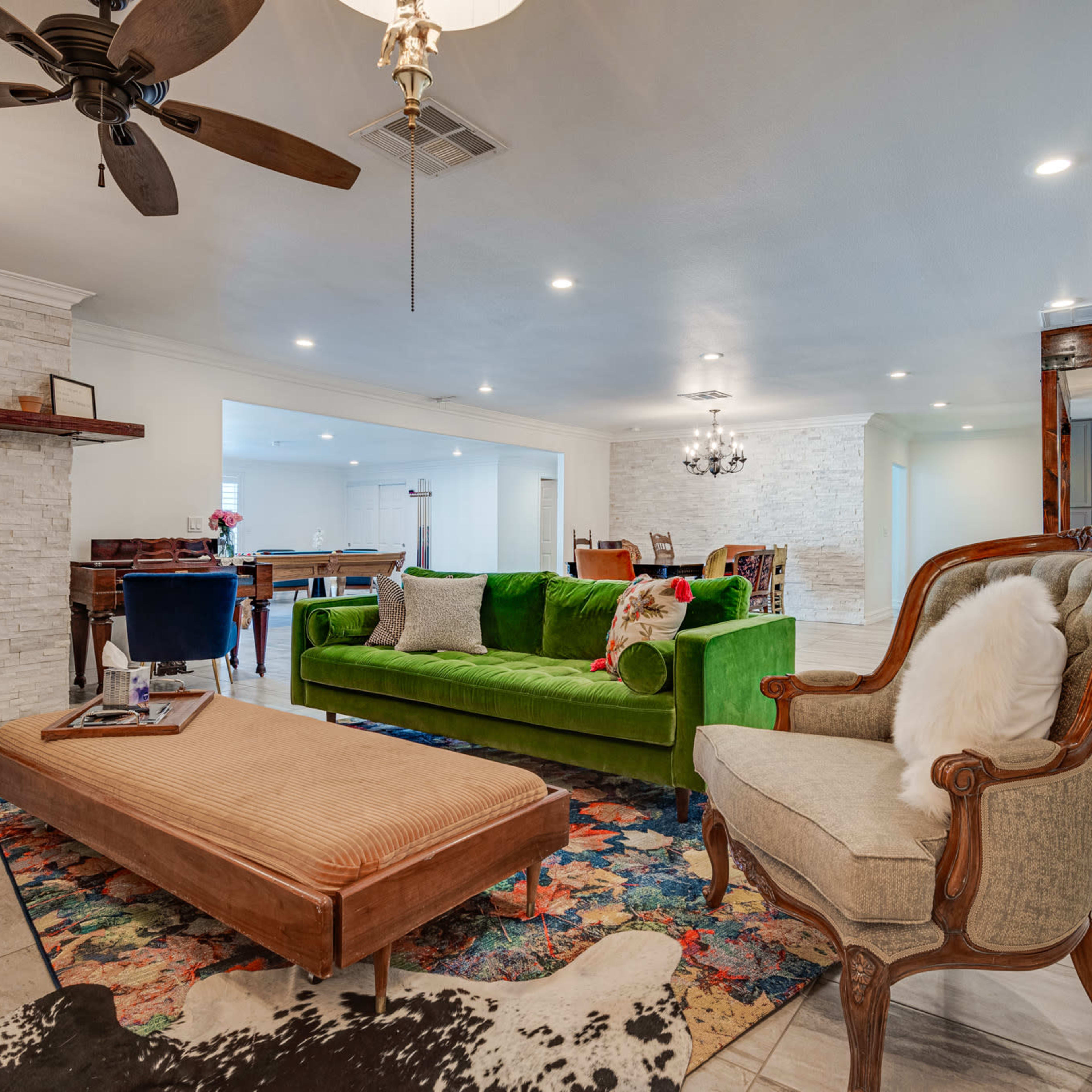 A bright living room featuring a green couch, a patterned rug, and a decorative coffee table, with a fireplace and an open layout leading to another space.
