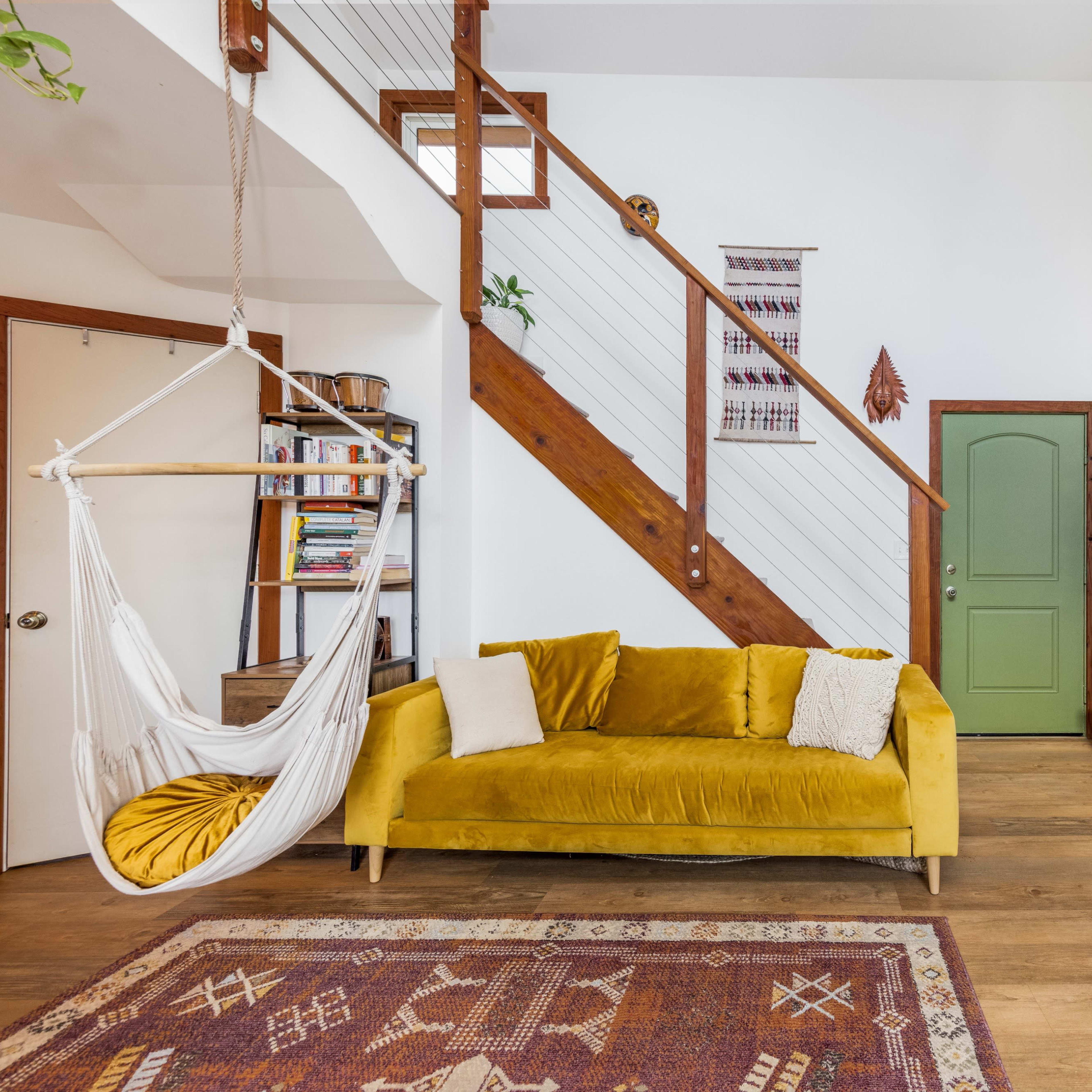 A cozy living room with a yellow couch, a hanging chair, a staircase, and a black wood-burning stove beside decorative tiles.