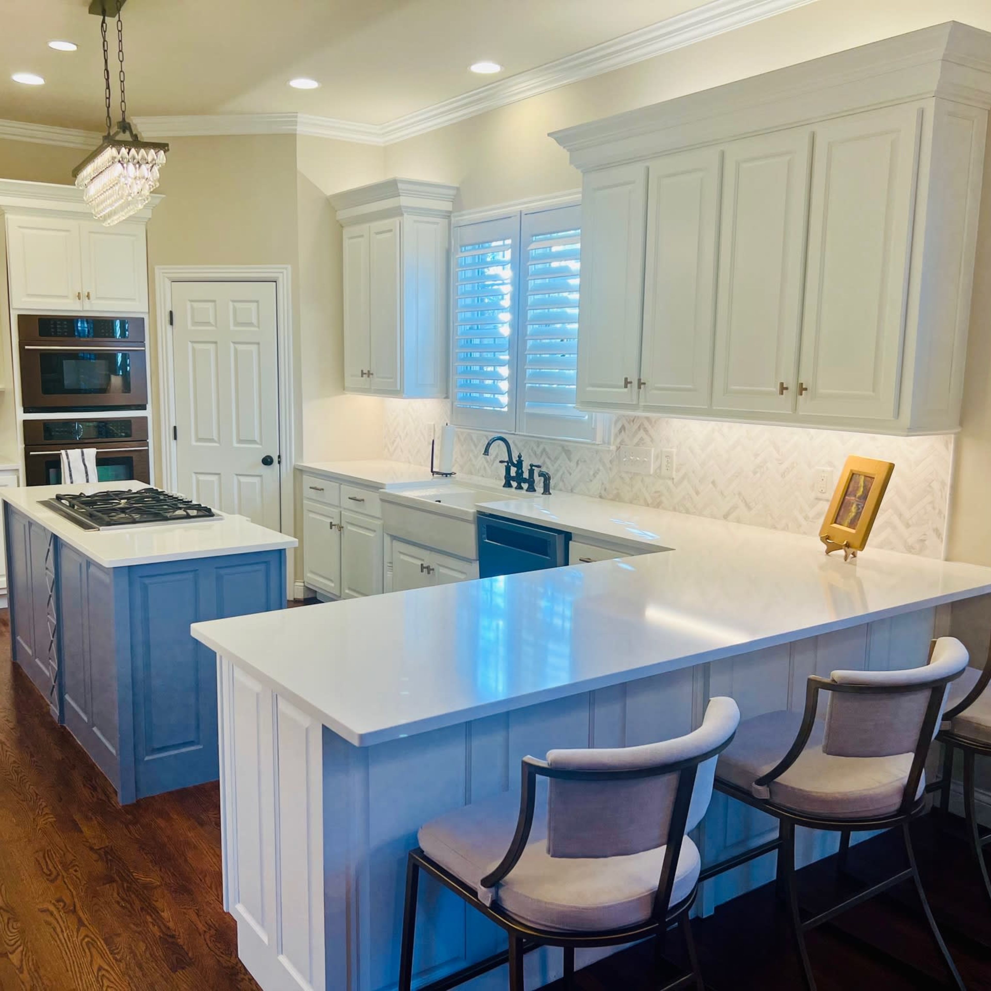 A modern kitchen with white cabinets, a blue island, a gas stove, and bar seating along a counter.