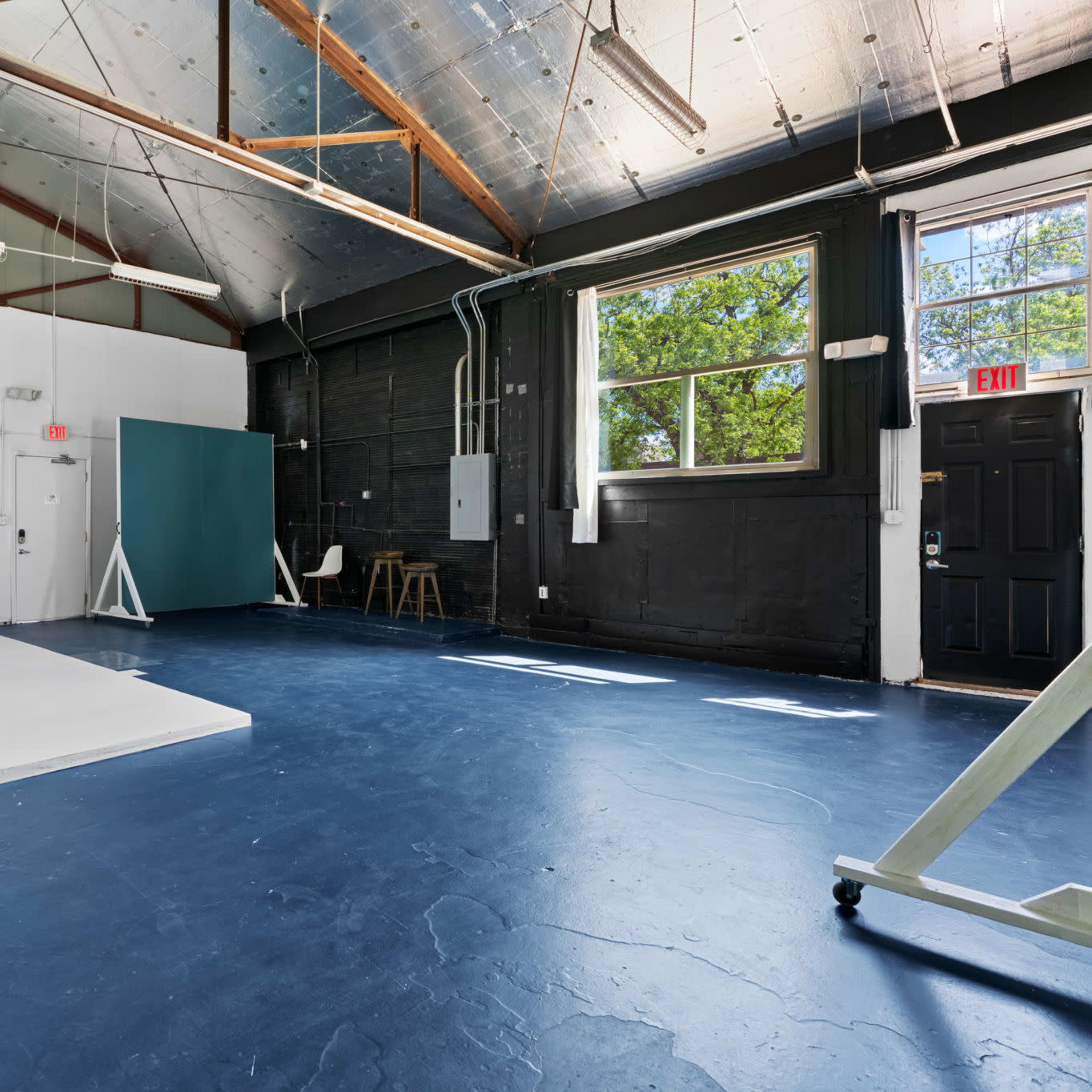 A spacious photography studio with a white backdrop, a blue floor, and several pieces of studio equipment.
