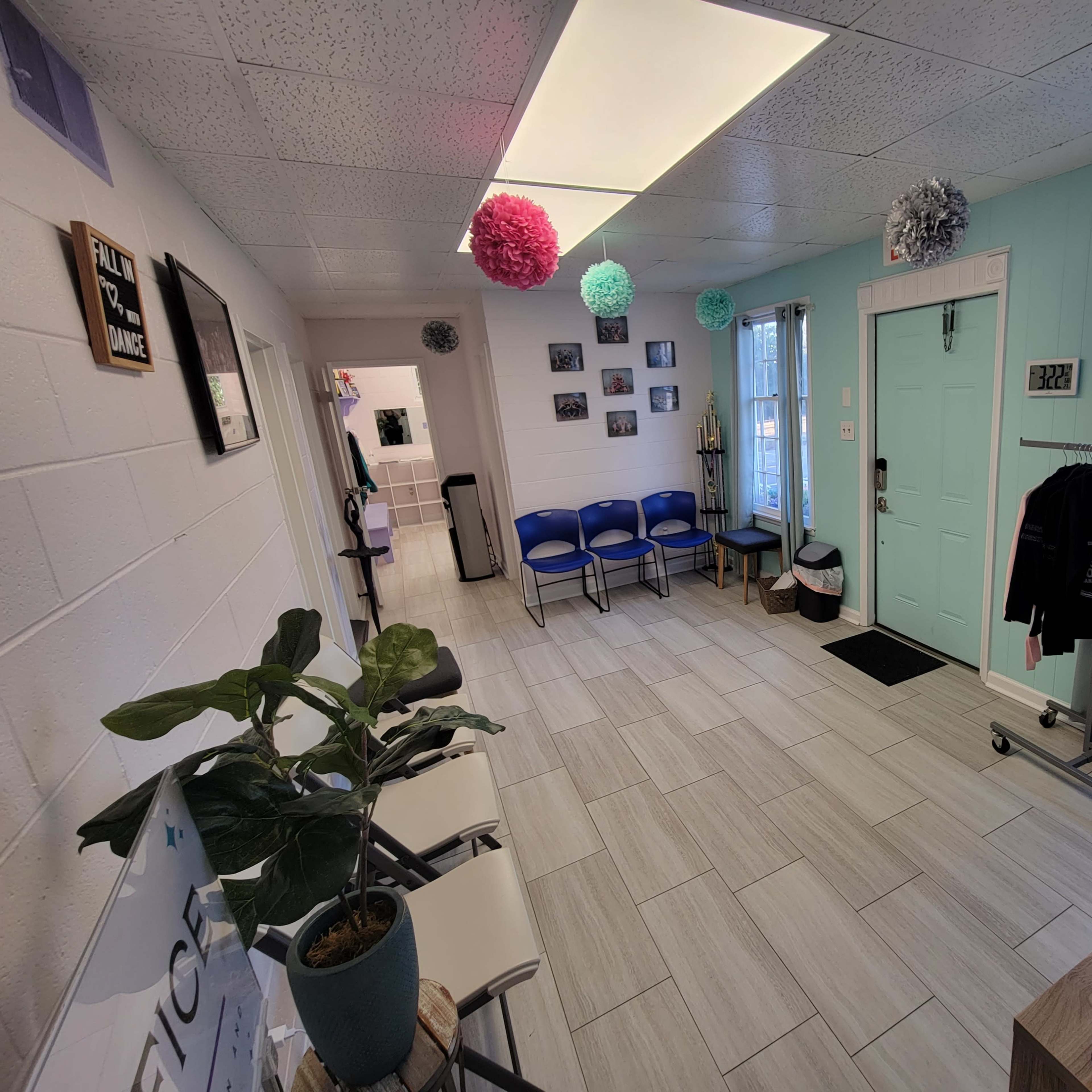 A bright waiting area with several blue chairs, a small plant, and a rack of clothing near the entrance.