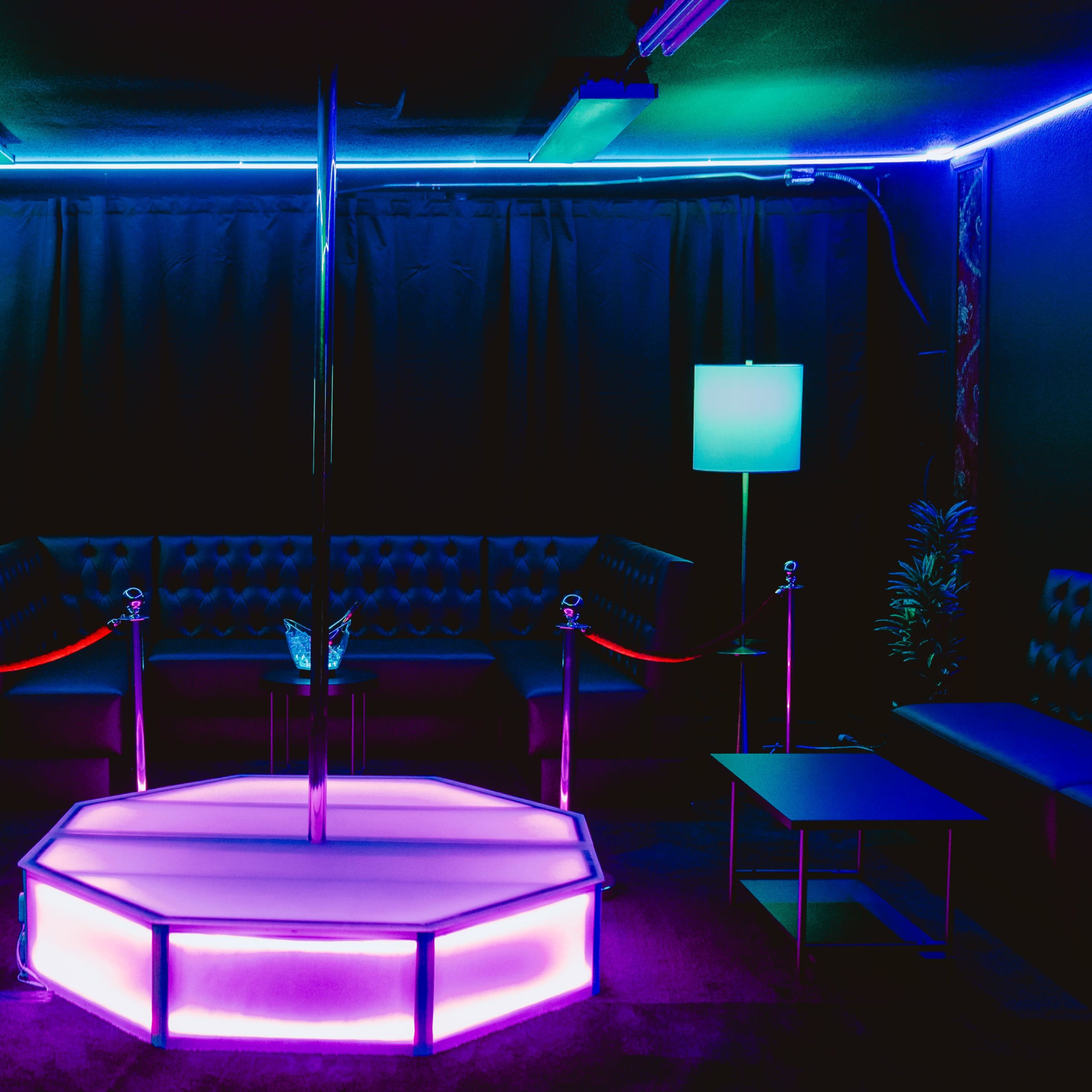 A dimly lit lounge area featuring a central illuminated pole on an octagonal platform, surrounded by seating and decorative lights.