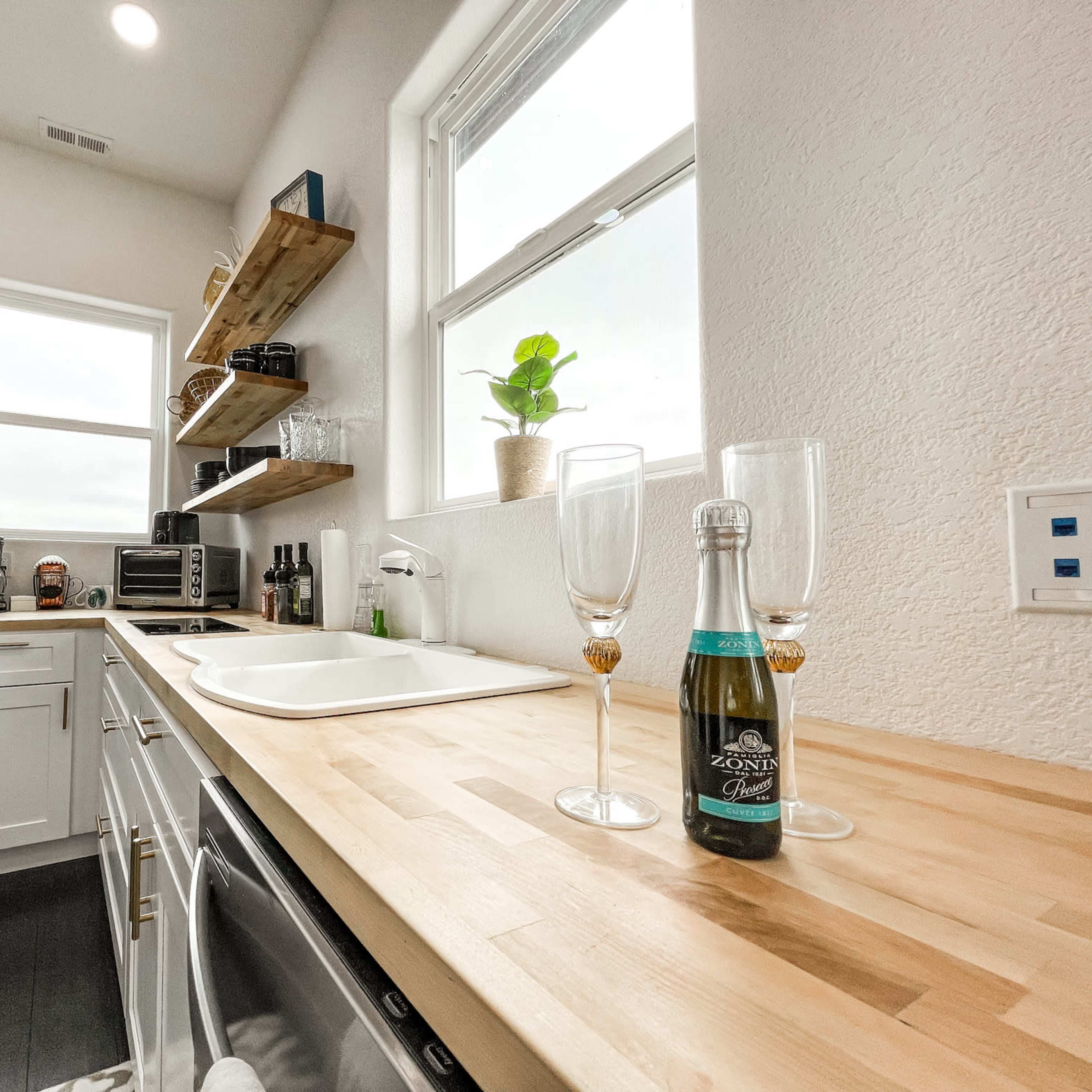 A well-organized kitchen featuring a stainless steel refrigerator, wooden countertop, and a bottle of sparkling wine with two glasses set nearby.