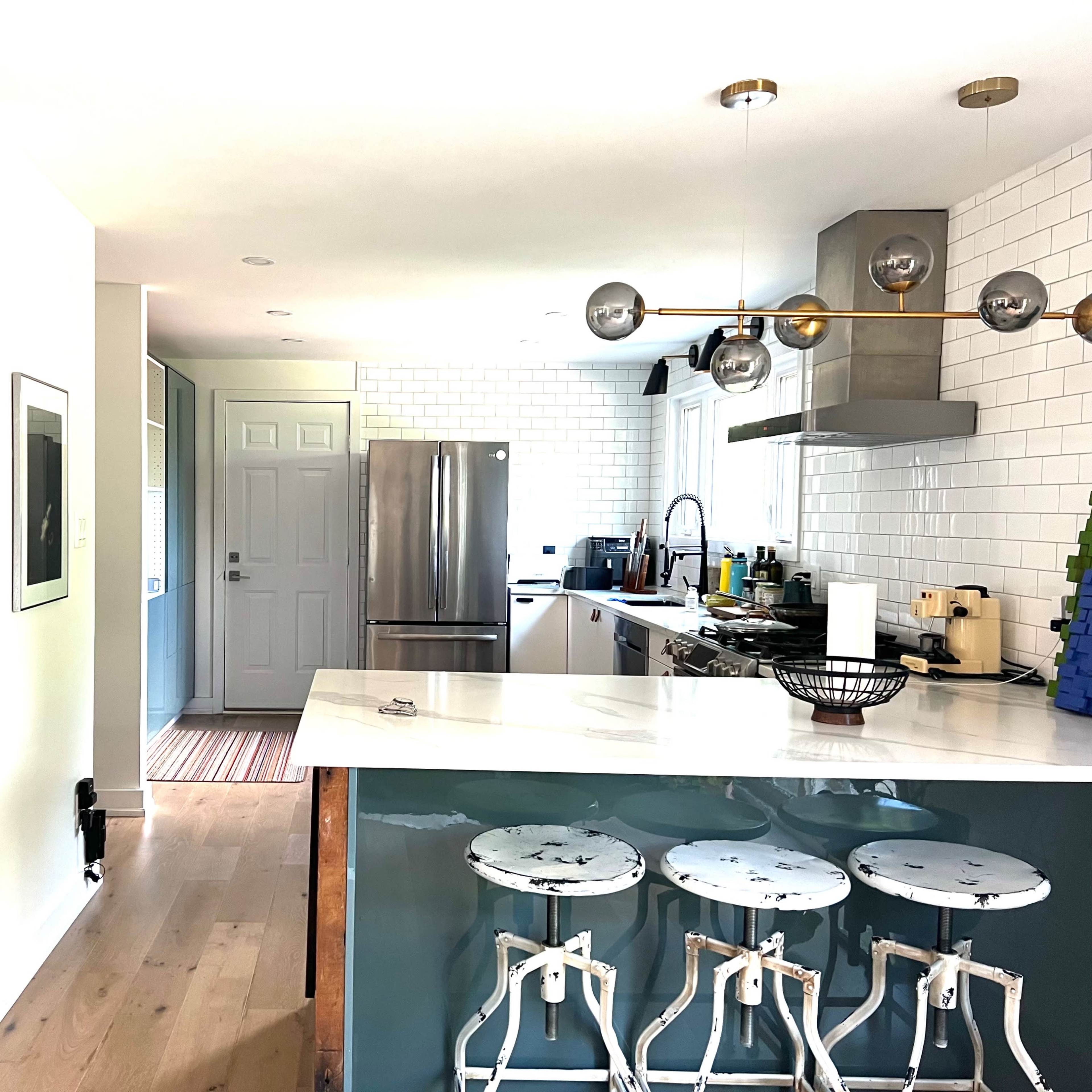 A modern kitchen features a sleek island with bar stools, stainless steel appliances, and a well-organized bar cart nearby.