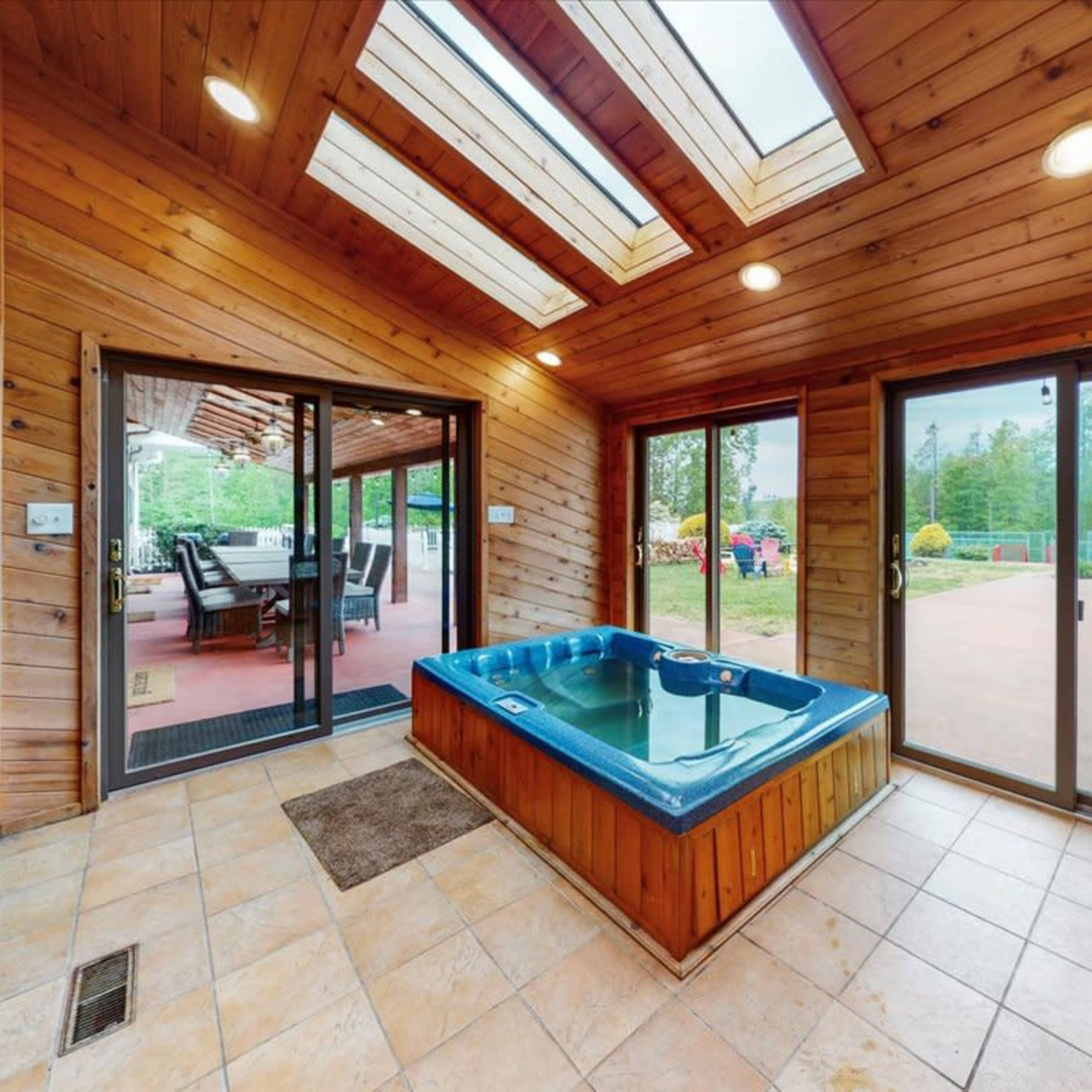A sunlit room featuring a hot tub surrounded by wooden walls, large windows, and sliding glass doors leading to an outdoor area.