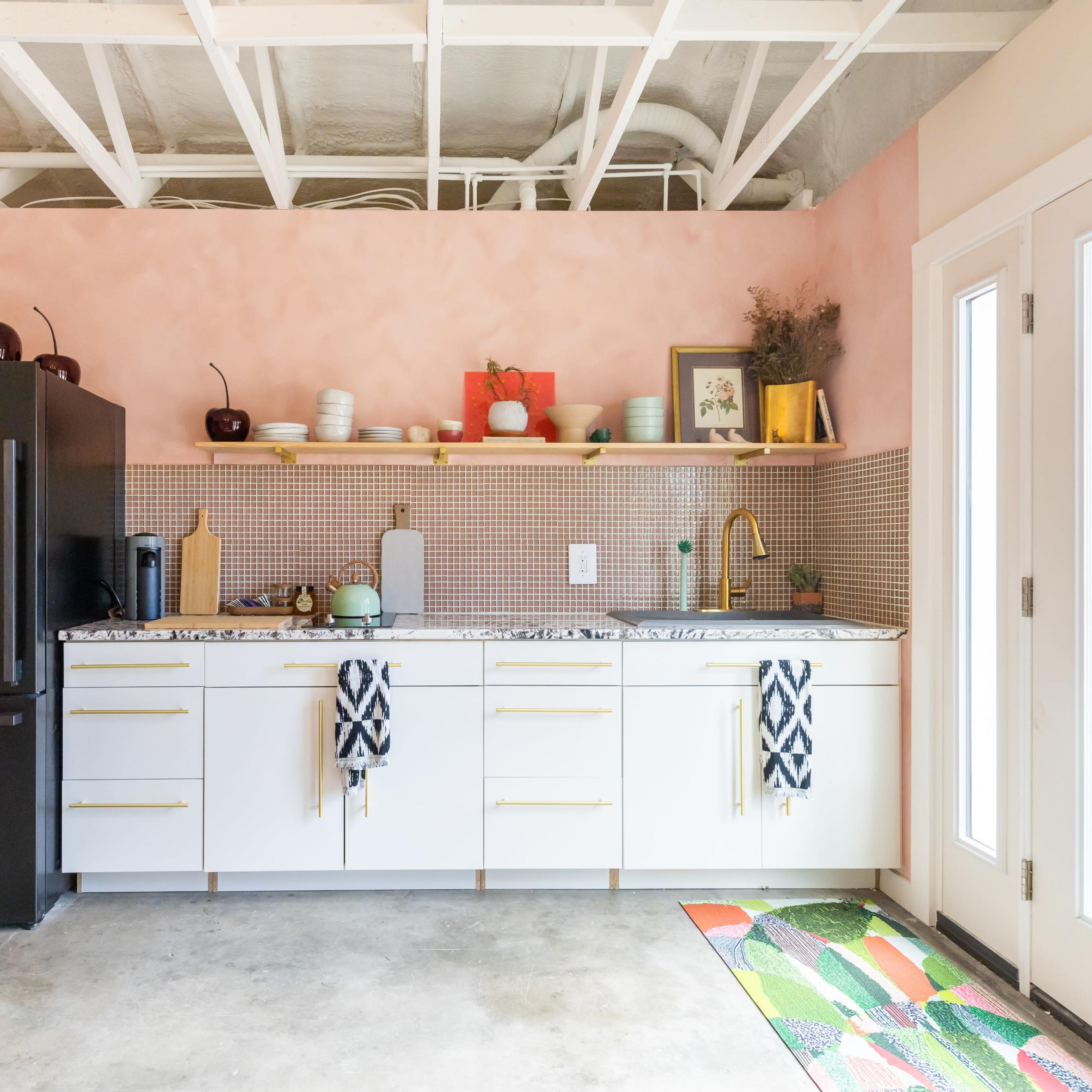 A modern kitchen with a pink wall, white cabinetry, a patterned backsplash, and a large black refrigerator.