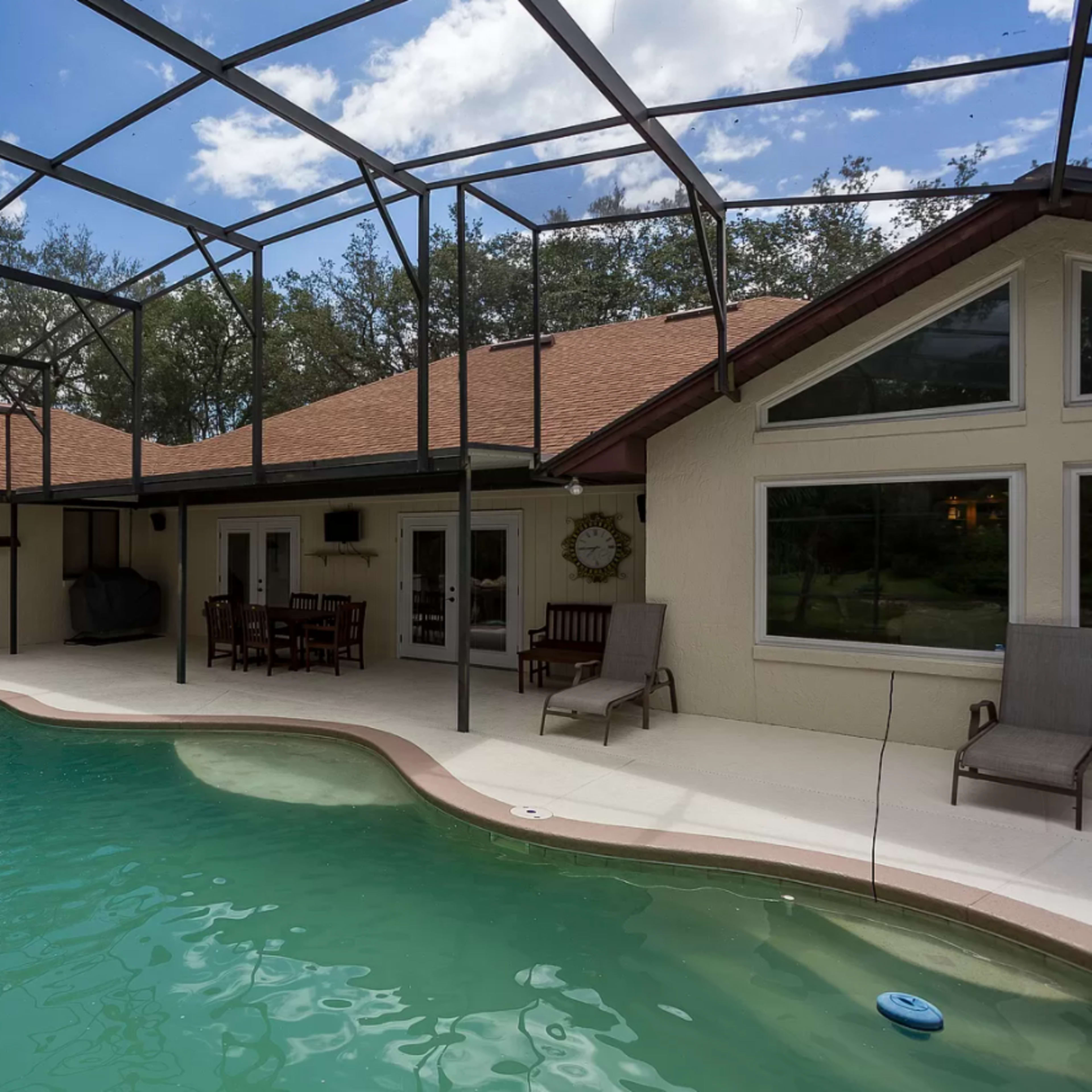 A backyard pool area enclosed by a screen, featuring a kidney-shaped pool, a rock waterfall, and a seating area with patio furniture.