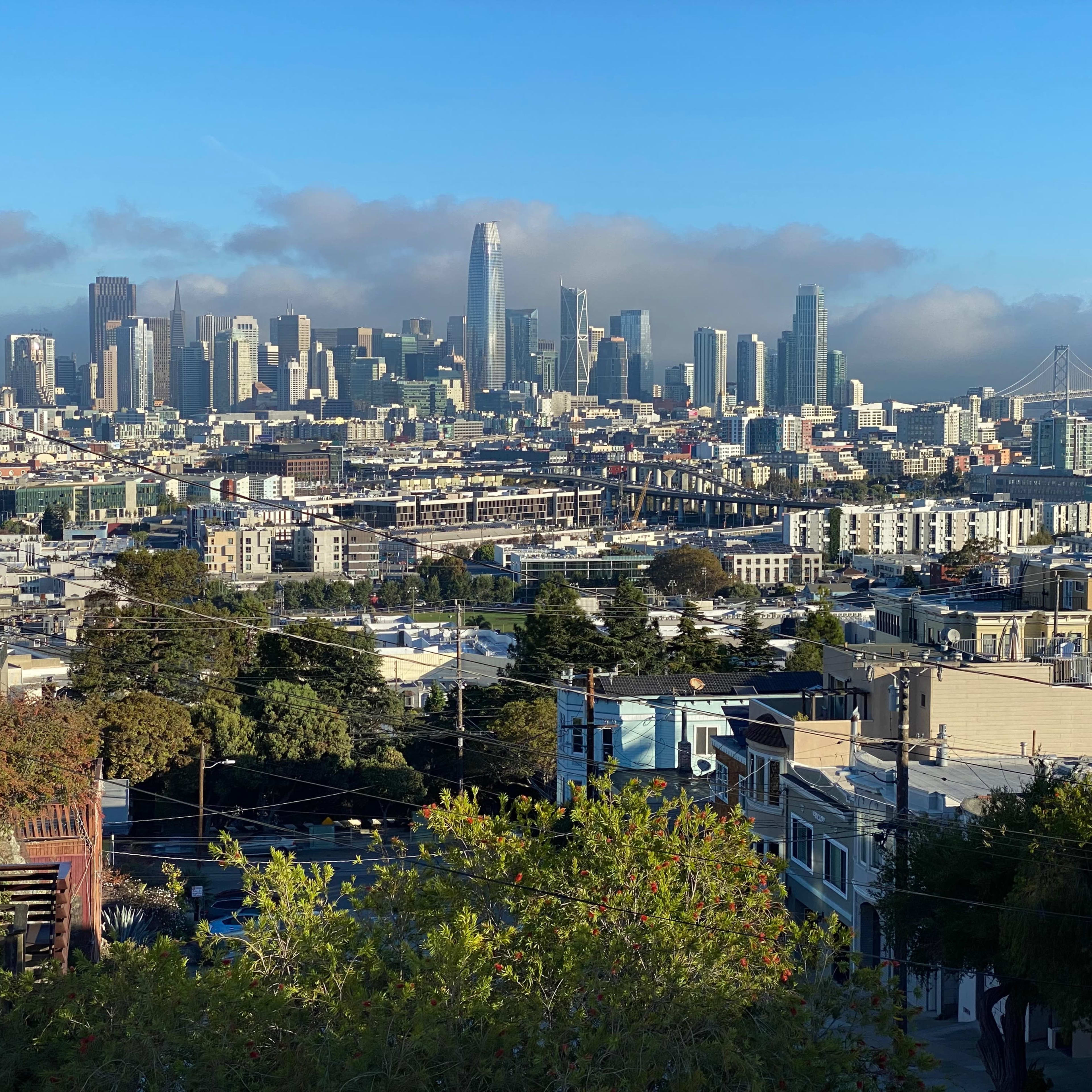 A panoramic view of the San Francisco skyline, featuring tall buildings and the Golden Gate Bridge in the background under a clear blue sky.