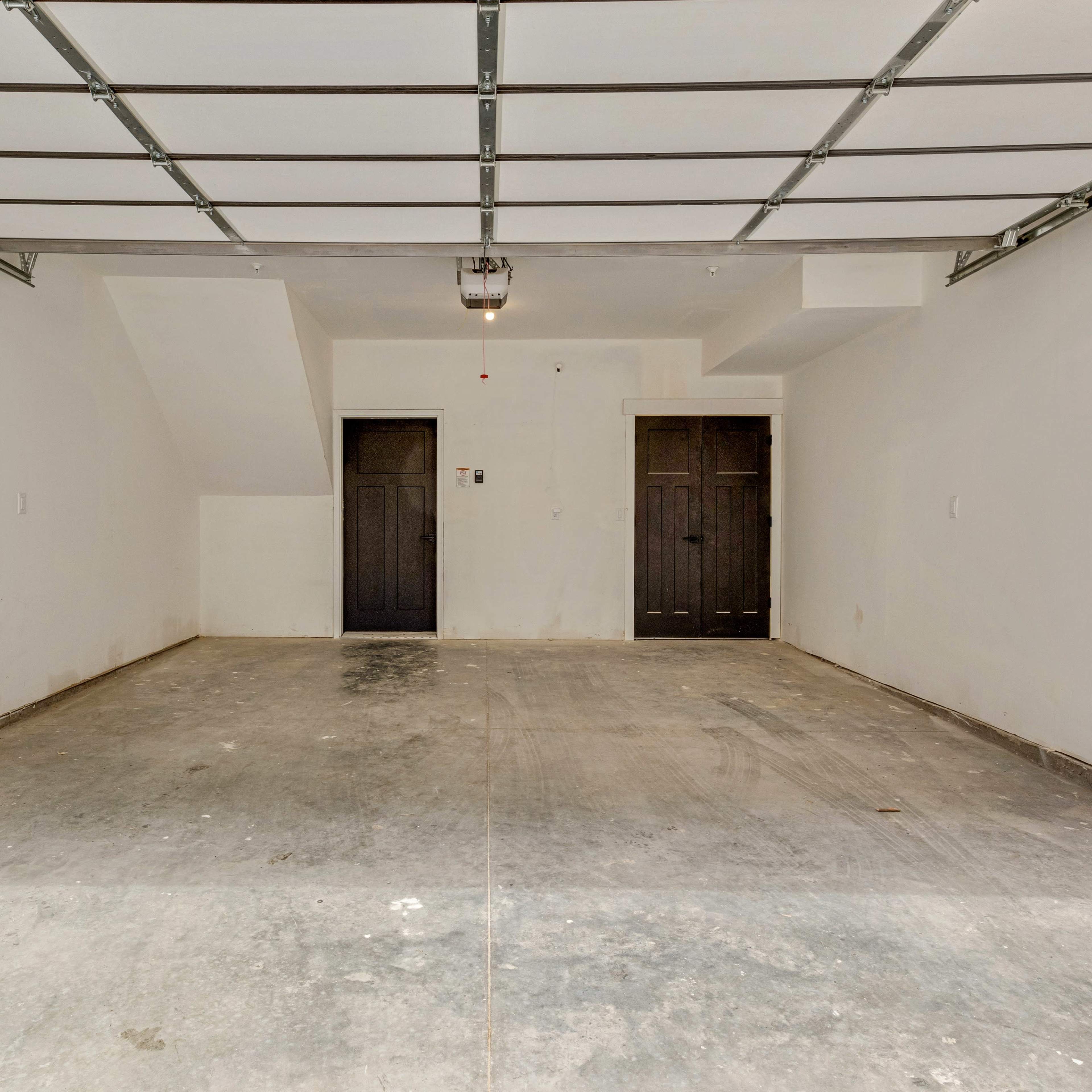 An empty garage space with a concrete floor and two dark doors on one wall.