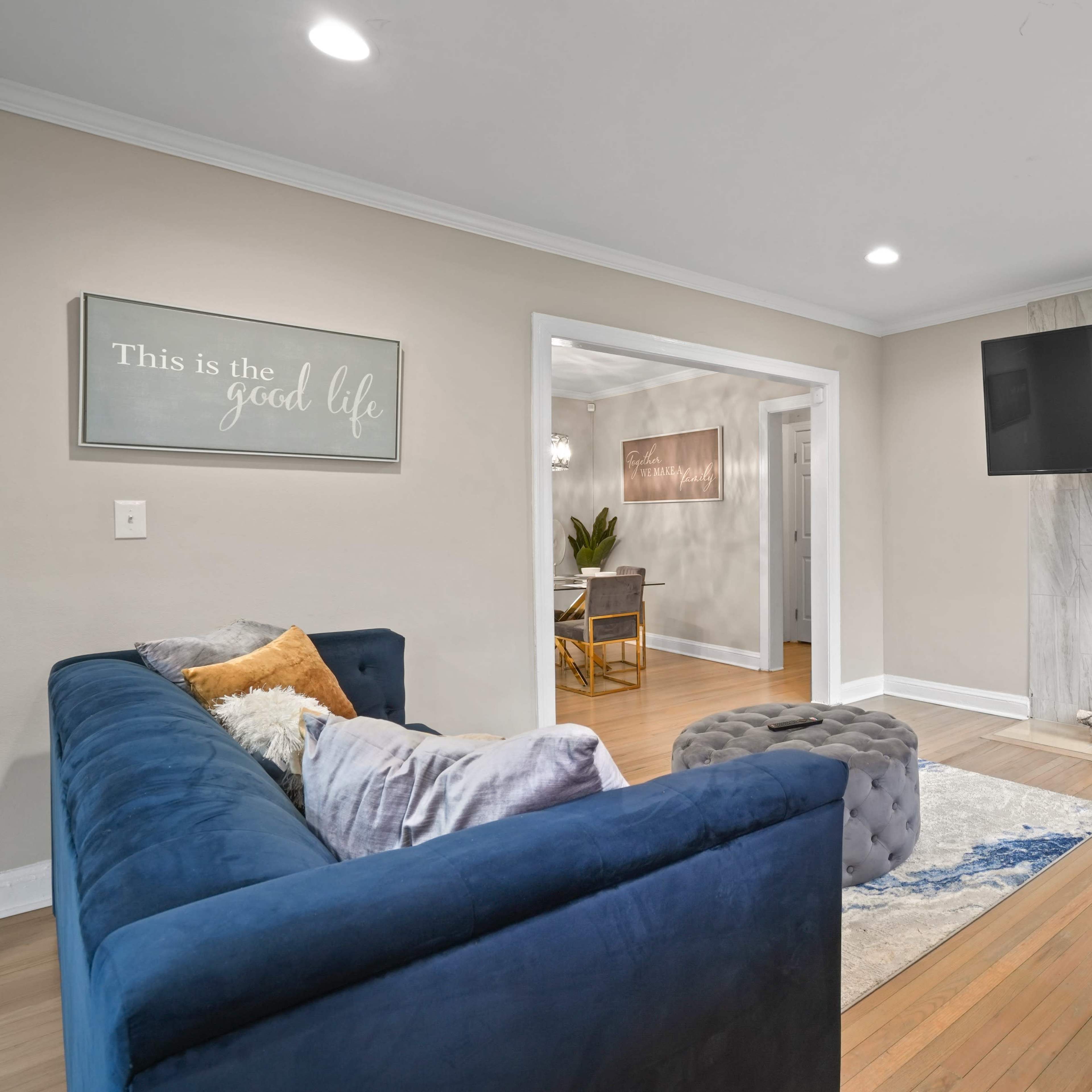 A modern living room features two blue sofas, a marble-accented wall with a mounted TV, and a view into an adjoining room with a dining area.