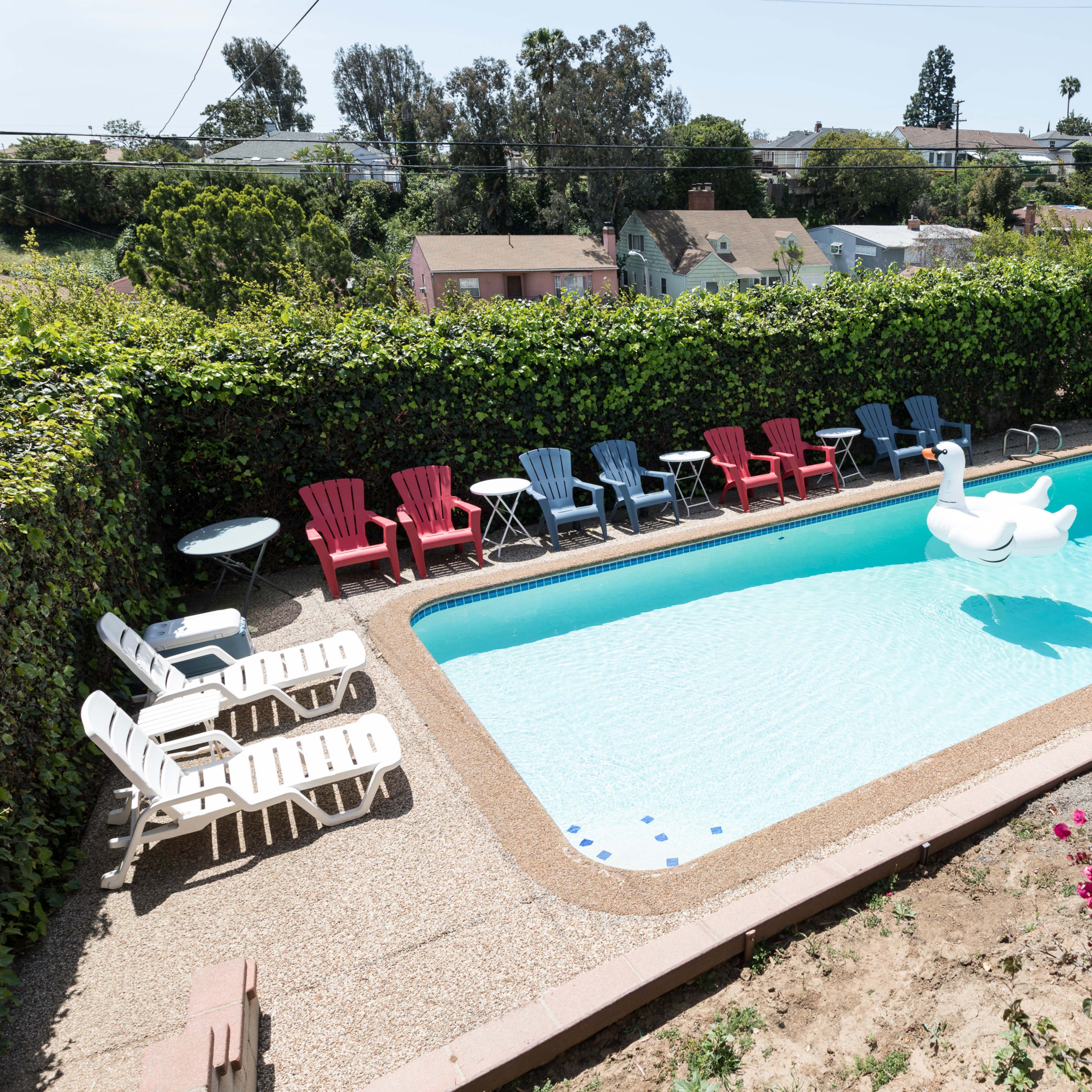 A swimming pool surrounded by colorful lounge chairs and a large inflatable swan float, set in a landscaped backyard.