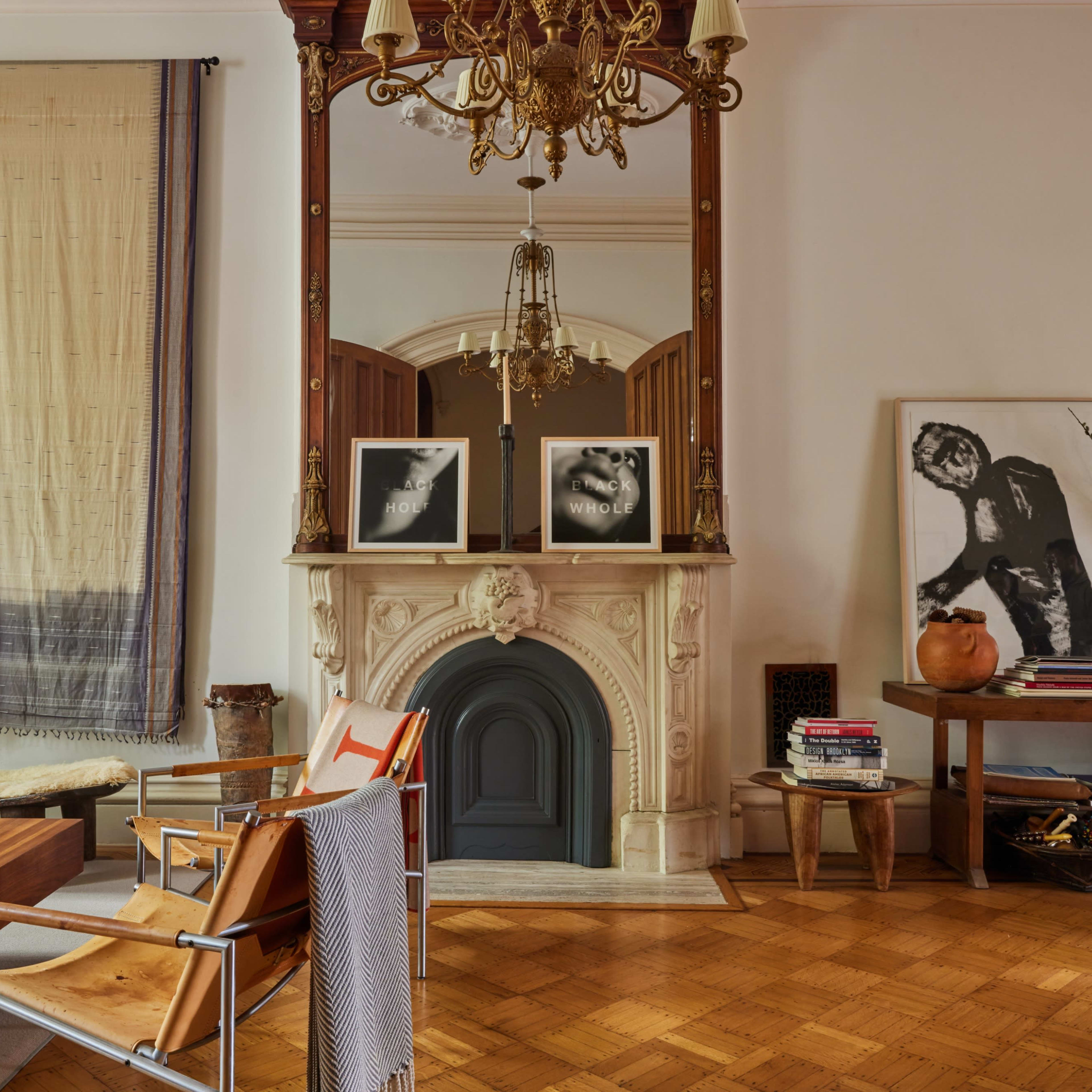 A stylish room featuring a fireplace with a large mirror above it, decorated with two framed pictures, alongside a wooden table and a chair.