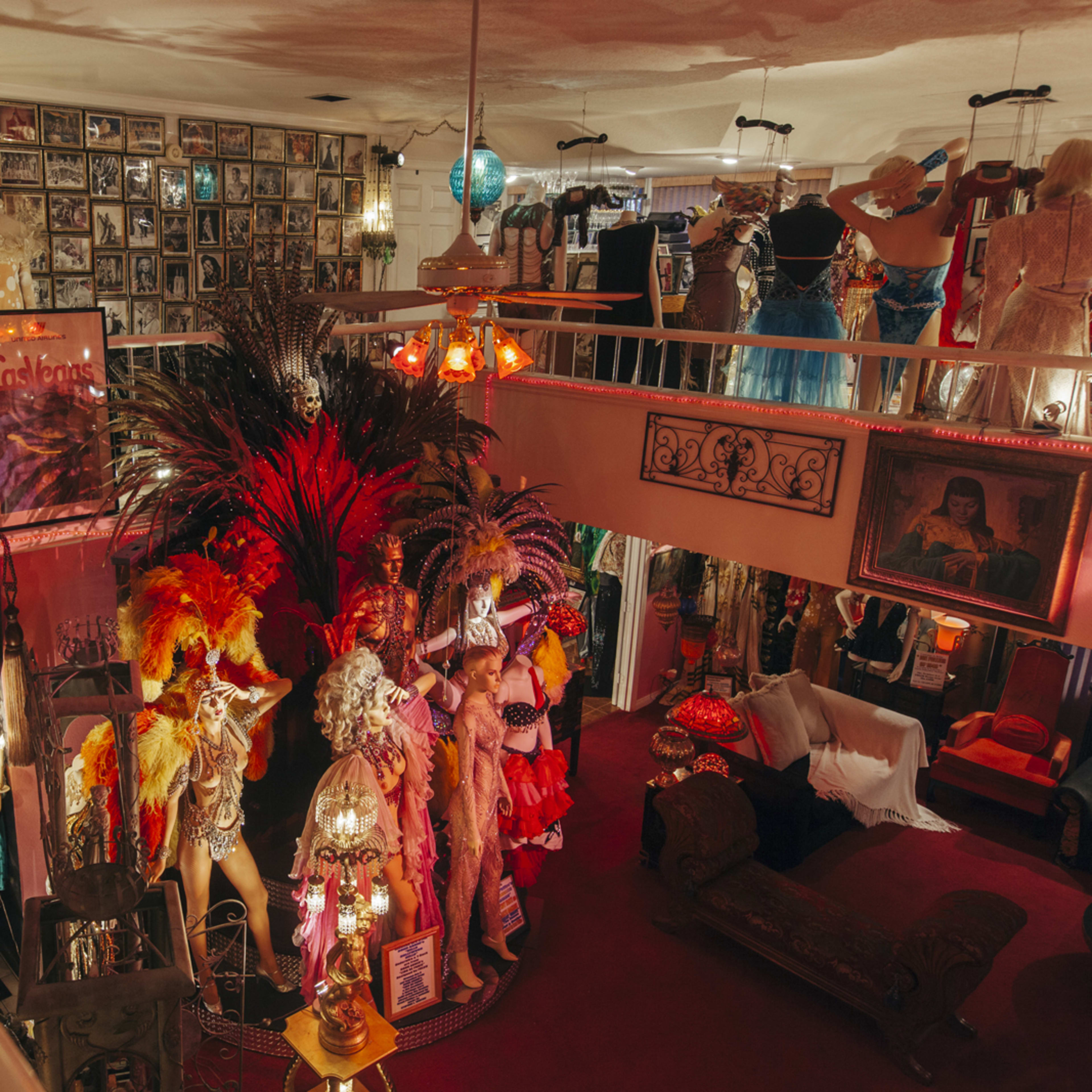 An eclectic vintage costume shop filled with colorful costumes, photographs on the walls, and decorative items arranged around a central display area.