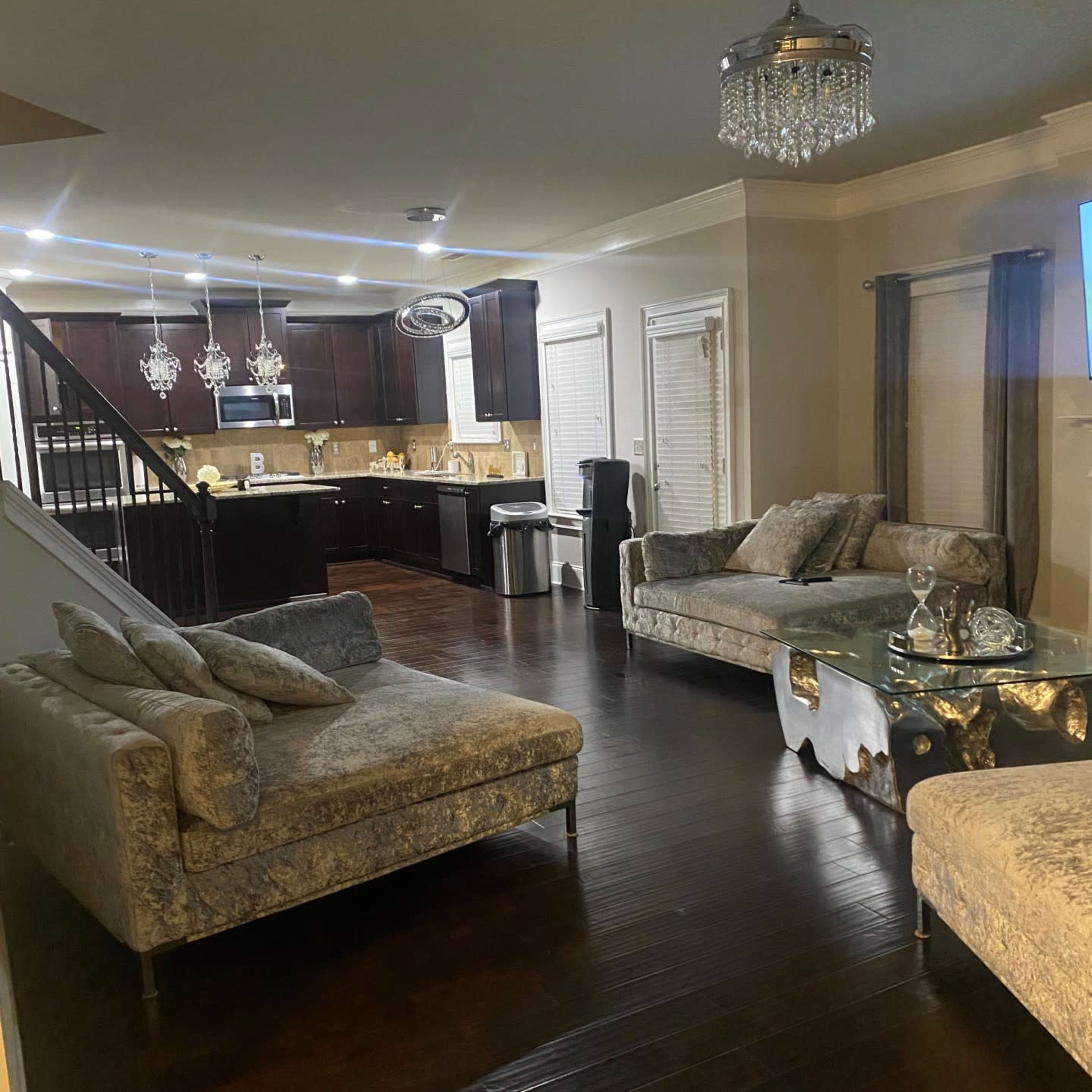 A living area with two velvet sofas facing a kitchen that features dark cabinetry and modern appliances.