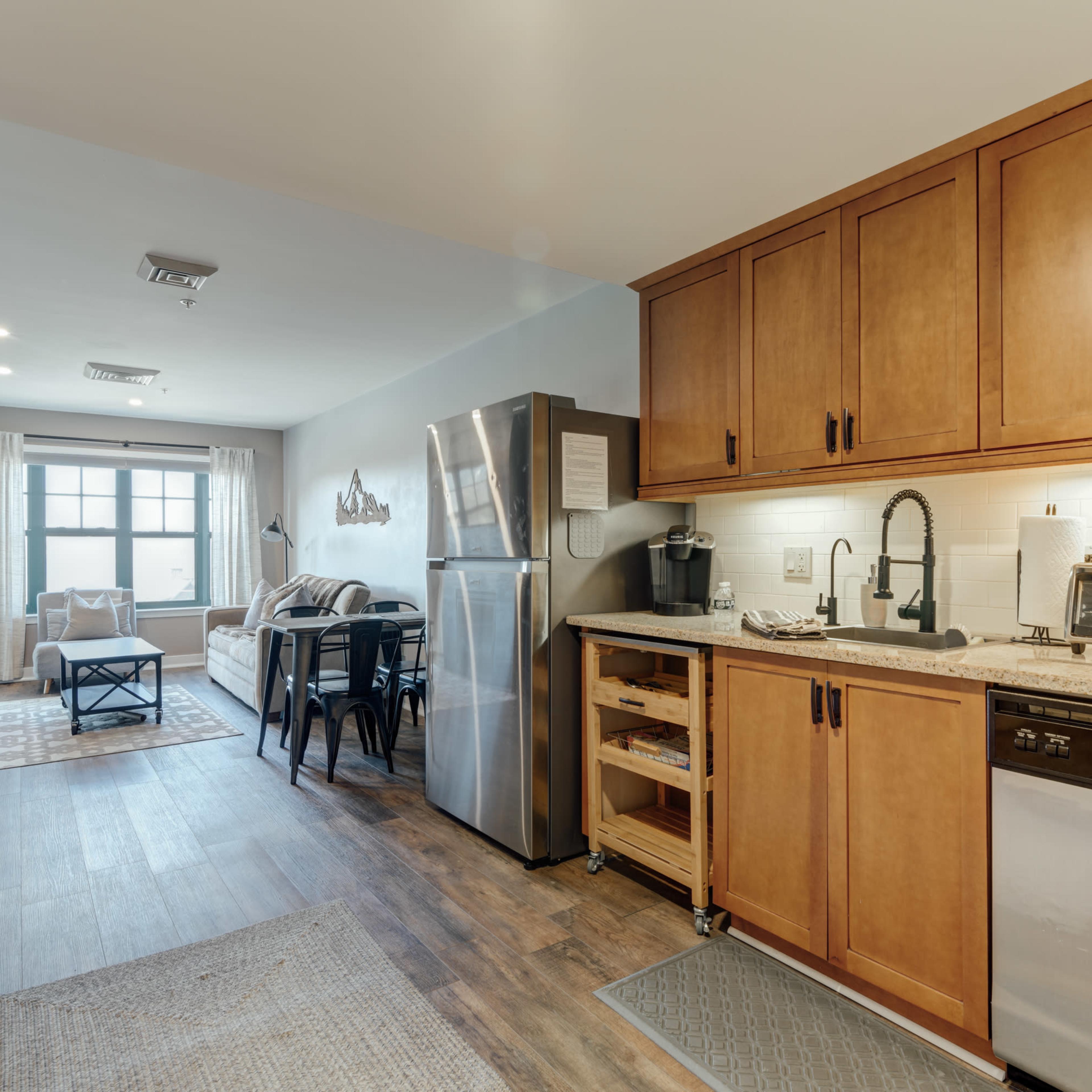 A modern kitchen with wooden cabinets and stainless steel appliances, adjacent to a dining area featuring a table and chairs.