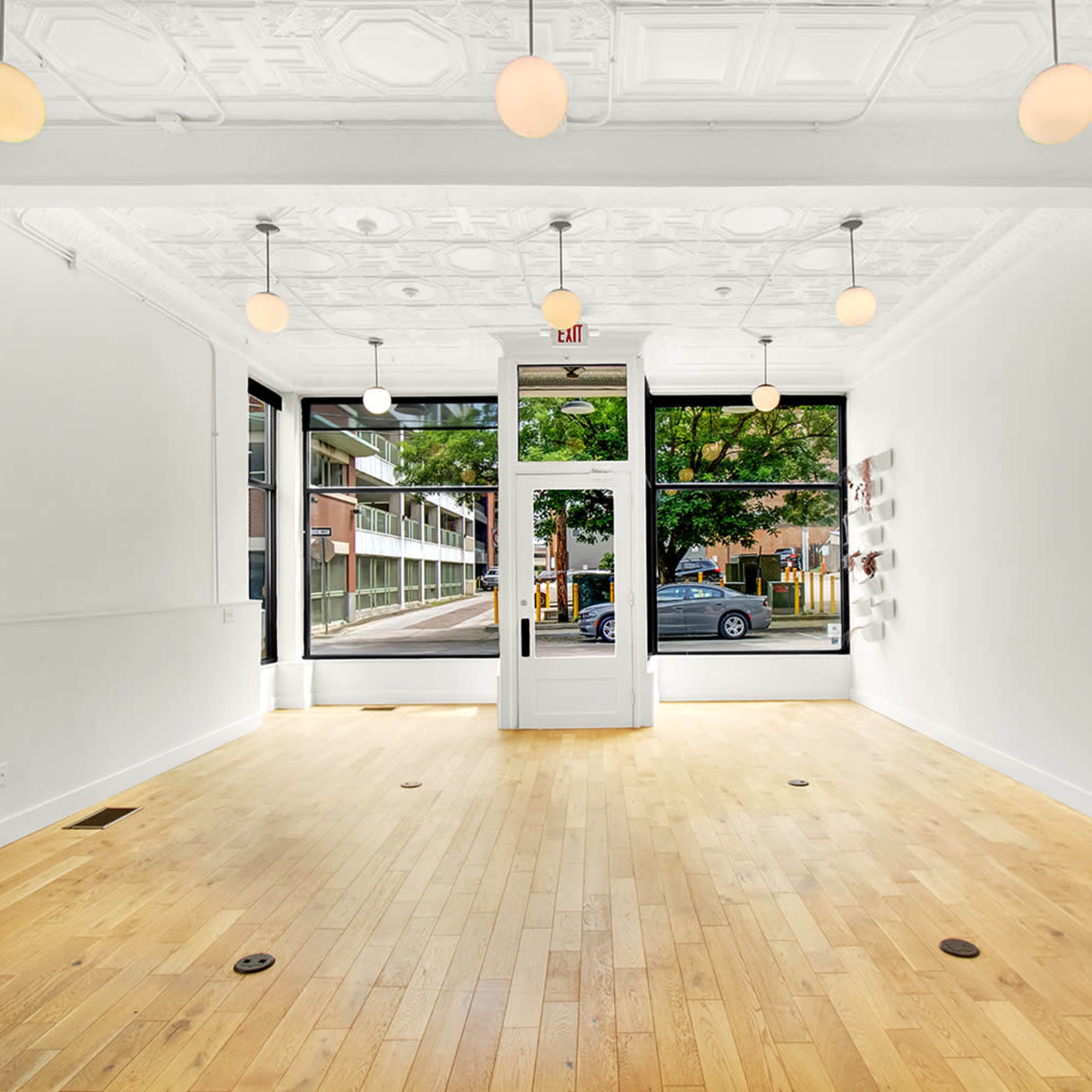 An empty, well-lit retail space with wooden floors and large windows facing the street.