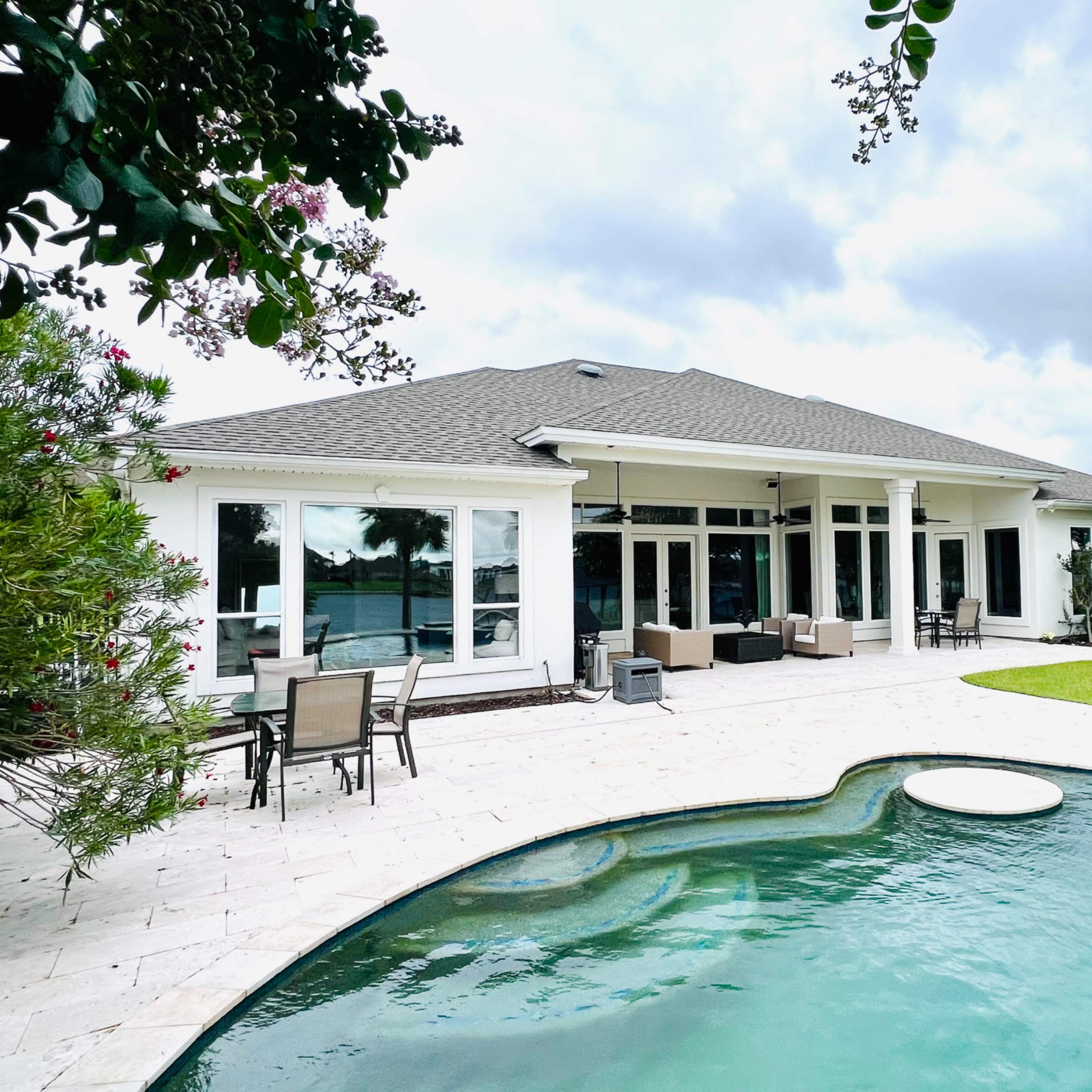 A modern house with large windows overlooking a swimming pool and landscaped yard on a cloudy day.