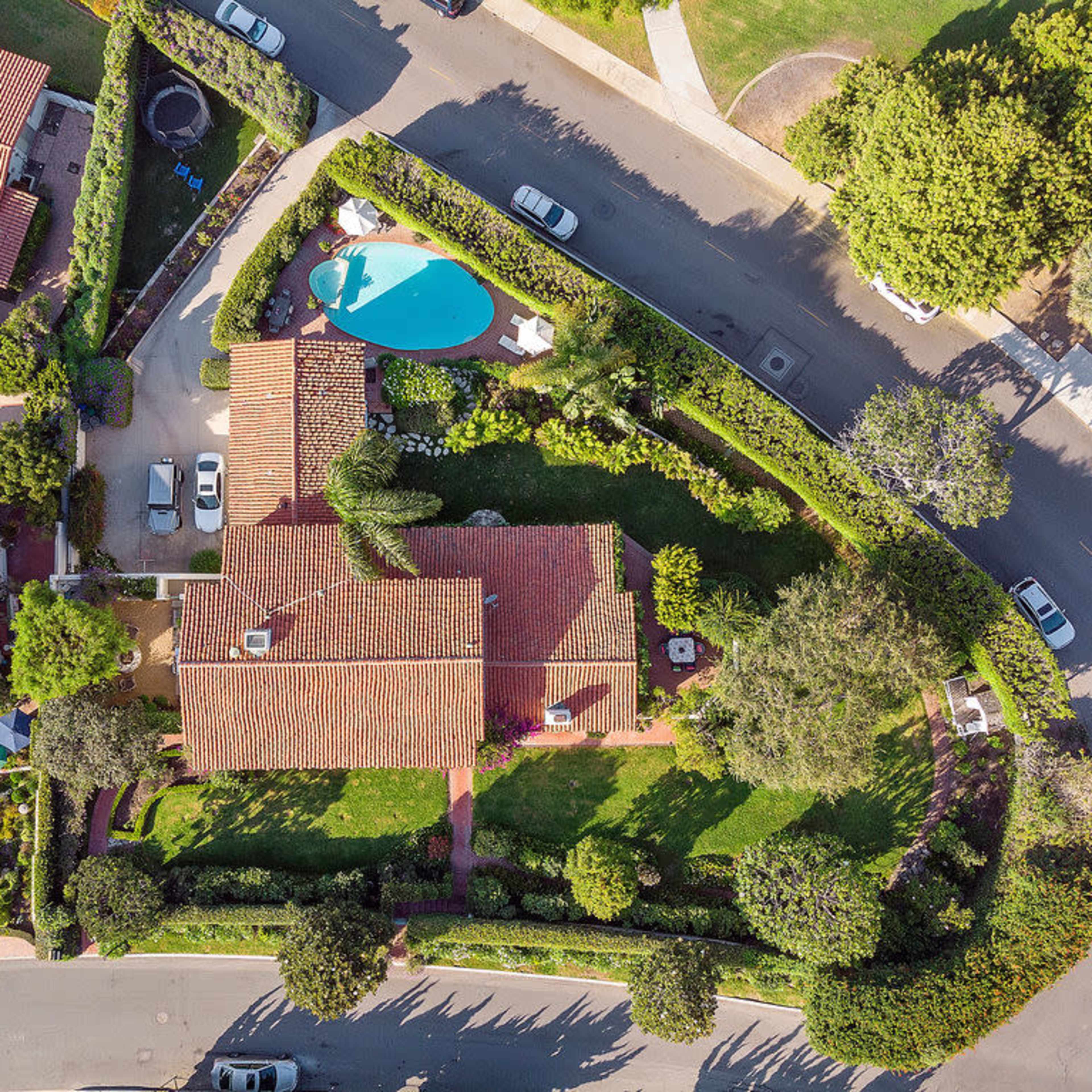 An aerial view of a residential property featuring a house with a red-tiled roof, surrounded by landscaped gardens and a swimming pool.