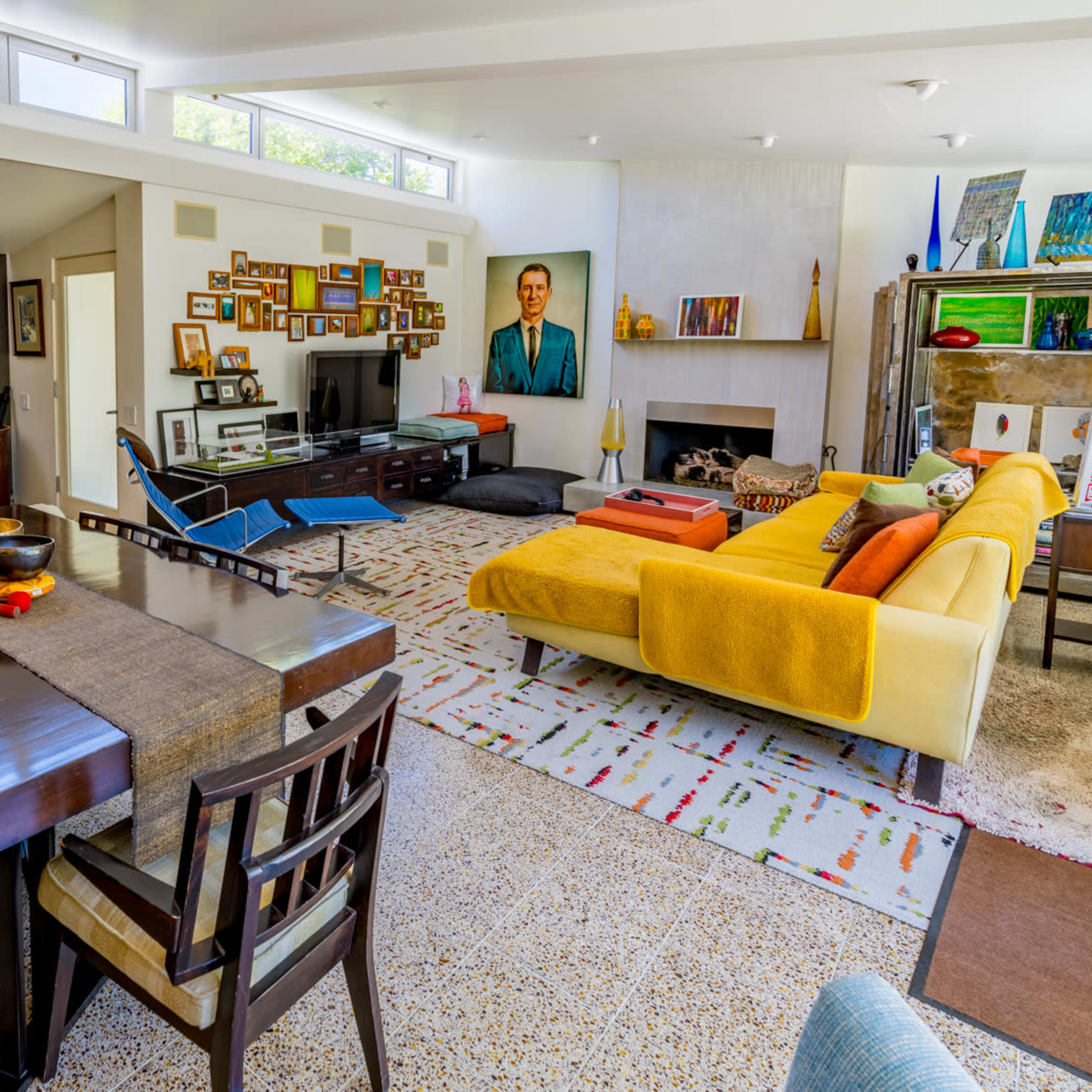 A spacious living area with a dining table, a yellow sofa, and various artworks on the walls.