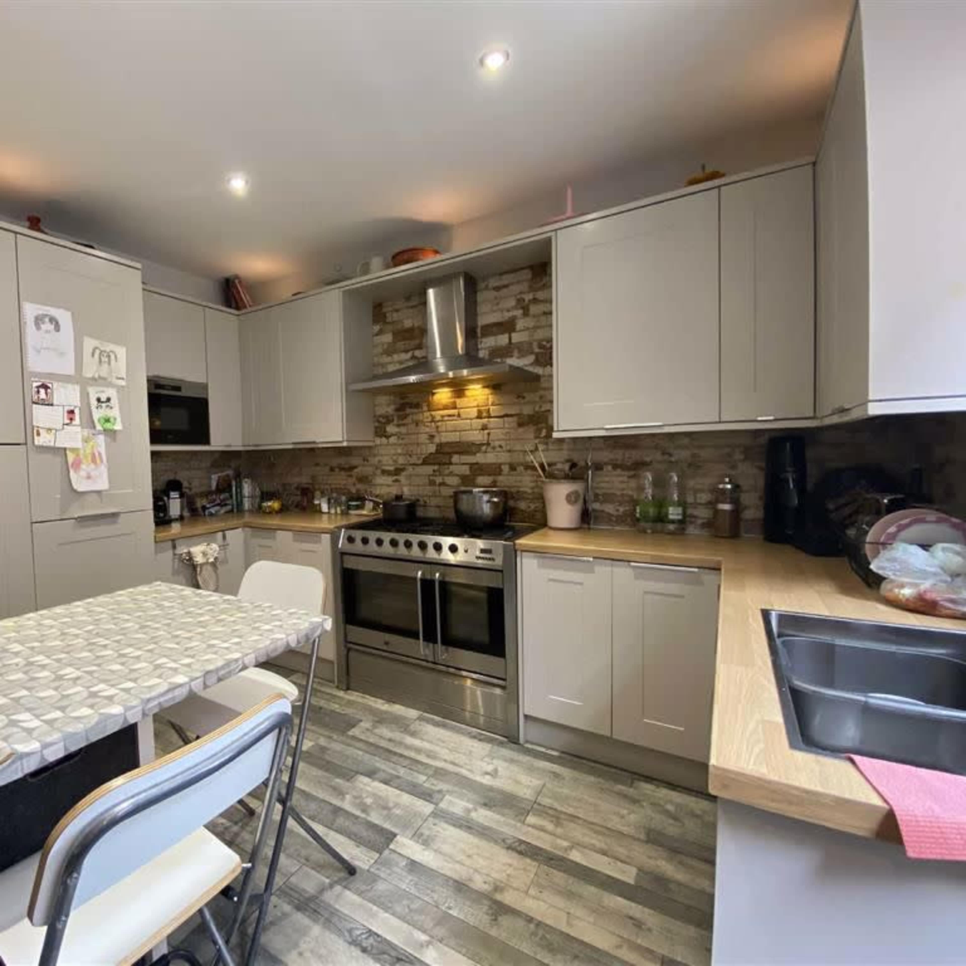 The kitchen features gray cabinetry, a tiled backsplash, a large stainless steel stove, and a table with chairs.