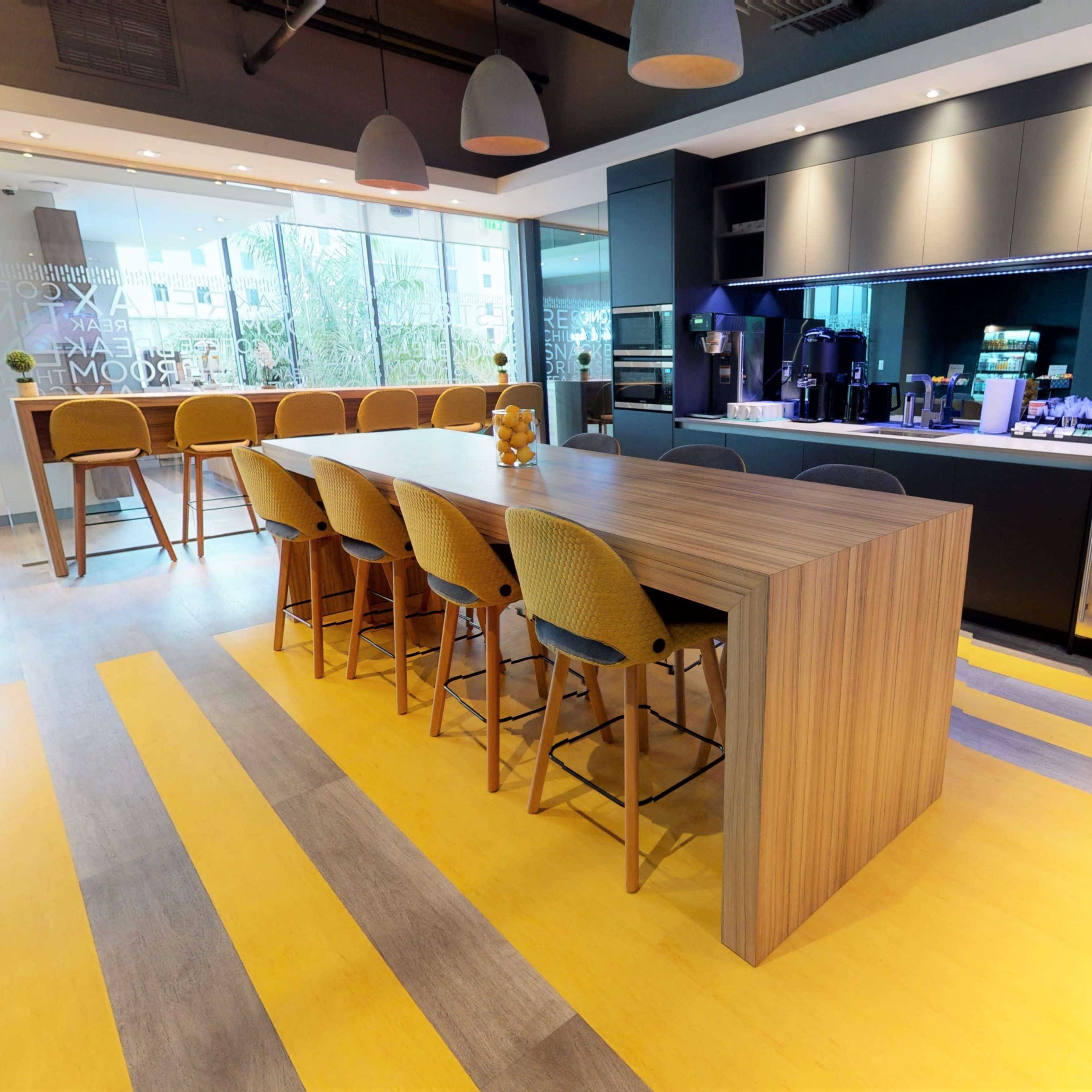A modern kitchen area featuring a long wooden bar with high stools, a sleek countertop, and stainless steel appliances.