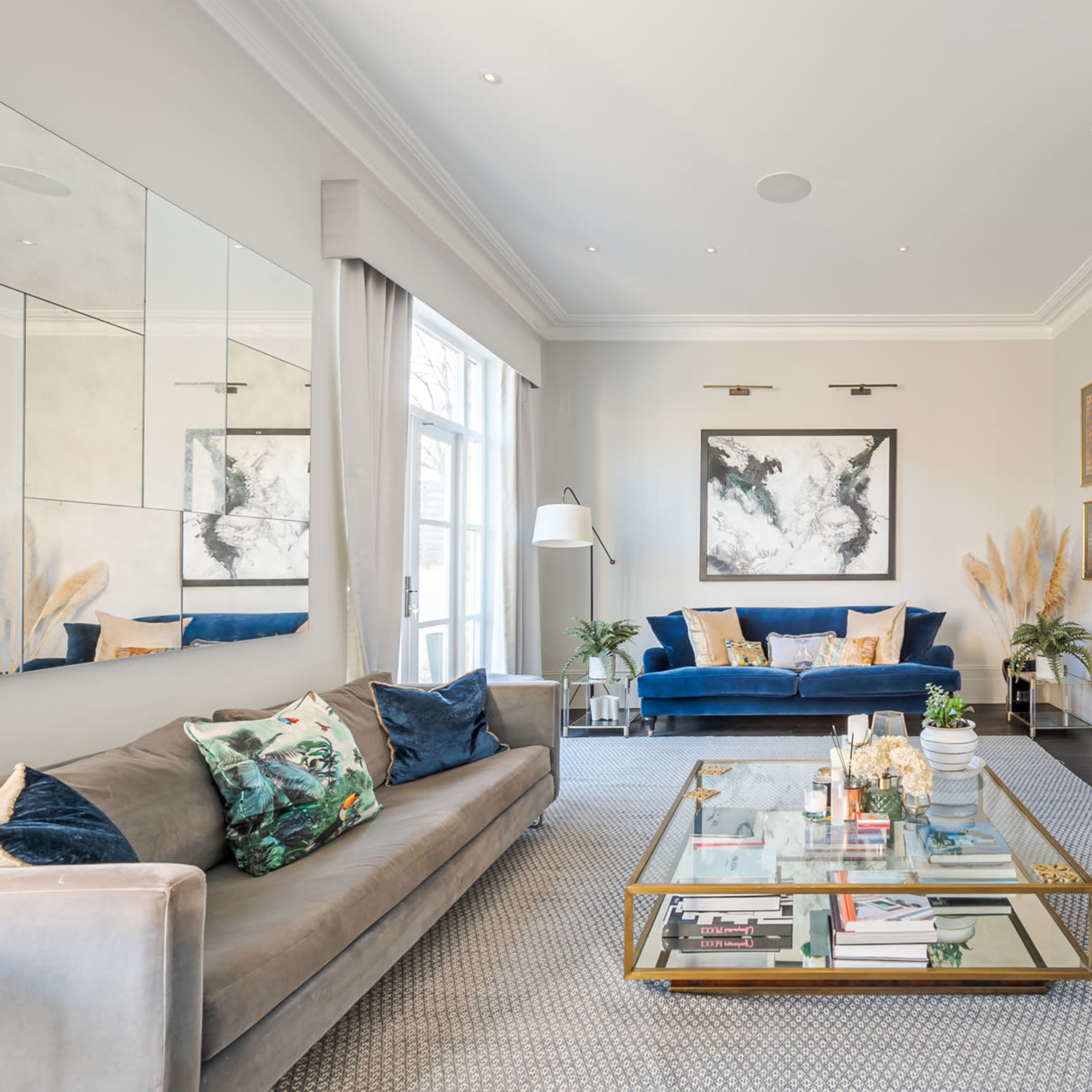 A stylish living room with a gray sofa, a blue accent chair, a coffee table with books and decorative items, and a modern fireplace.