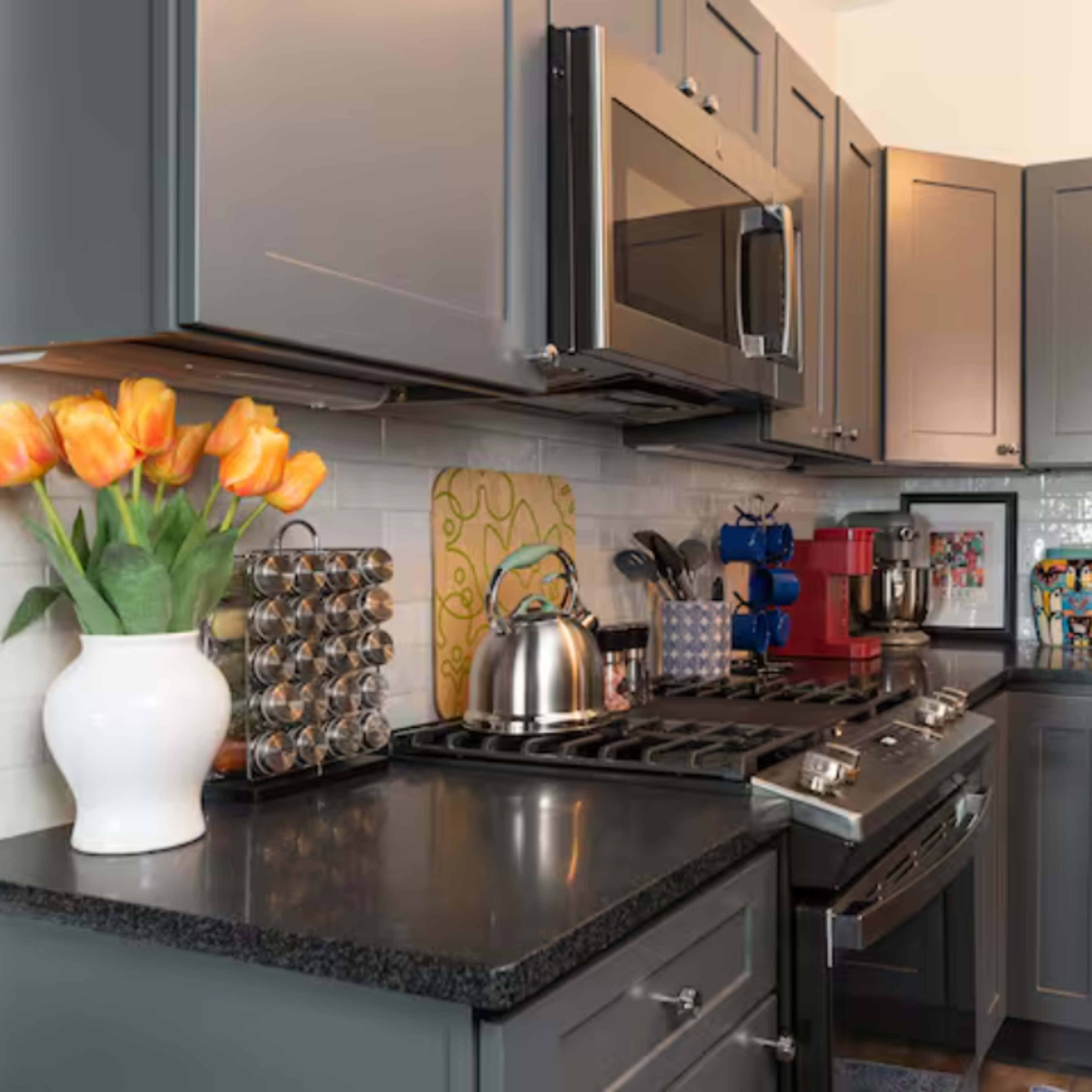 The kitchen features dark gray cabinets, a stainless steel microwave, and a gas stove, with a vase of tulips on the counter and various kitchen appliances neatly arranged.