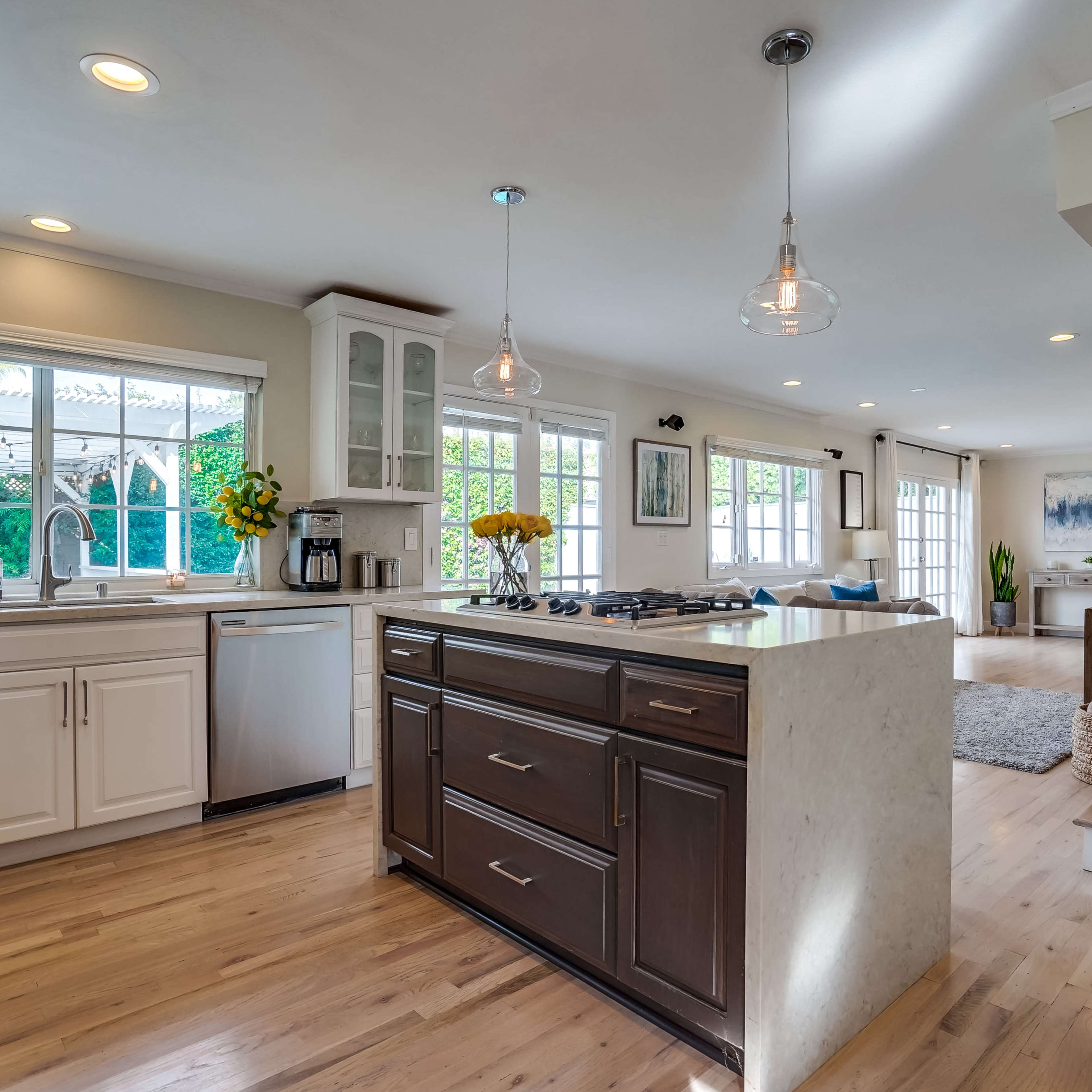 A modern kitchen featuring an island with a stovetop, white cabinetry, and large windows allowing natural light to enter.