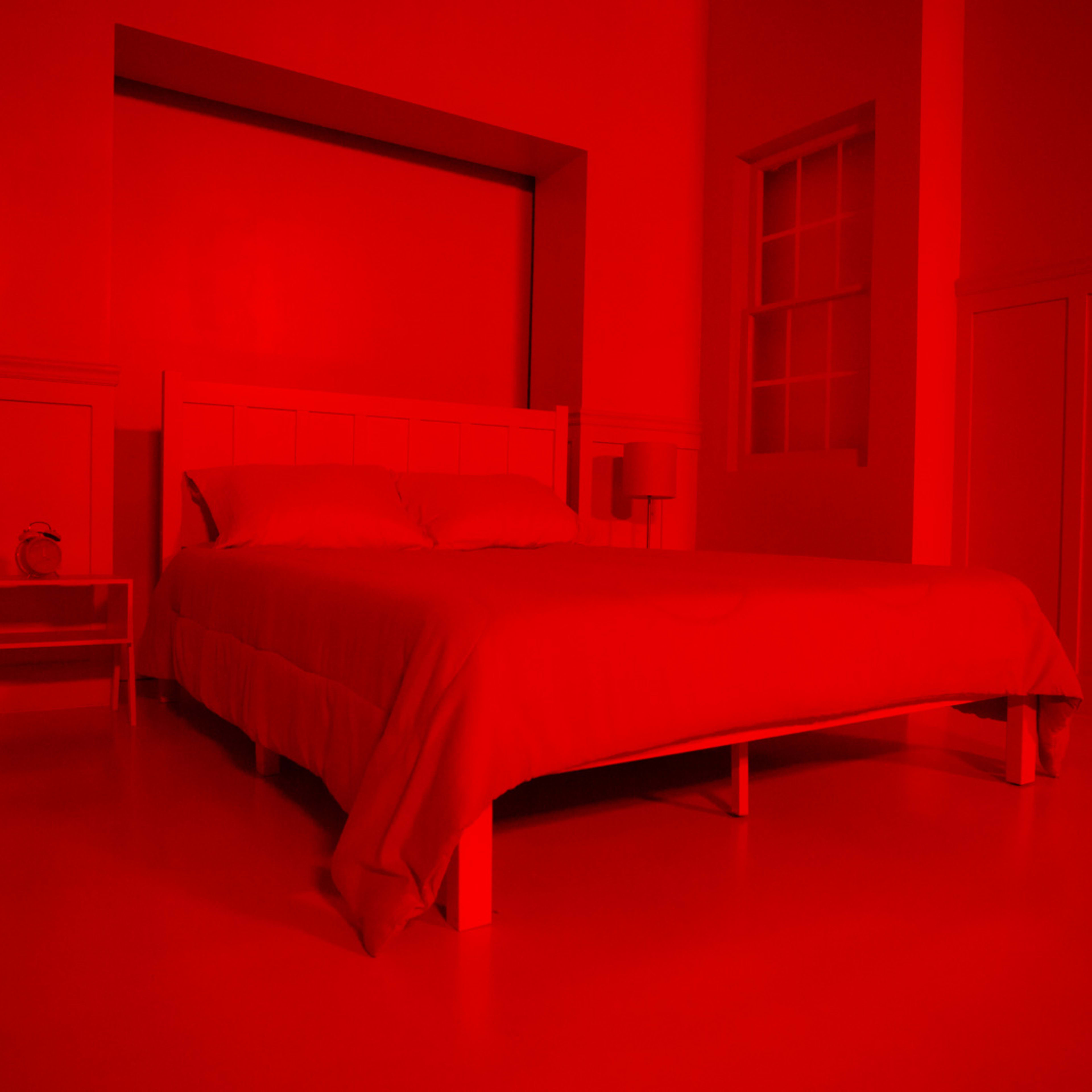 A bedroom with a white bed and furniture, illuminated by a red light, creating a monochromatic atmosphere.
