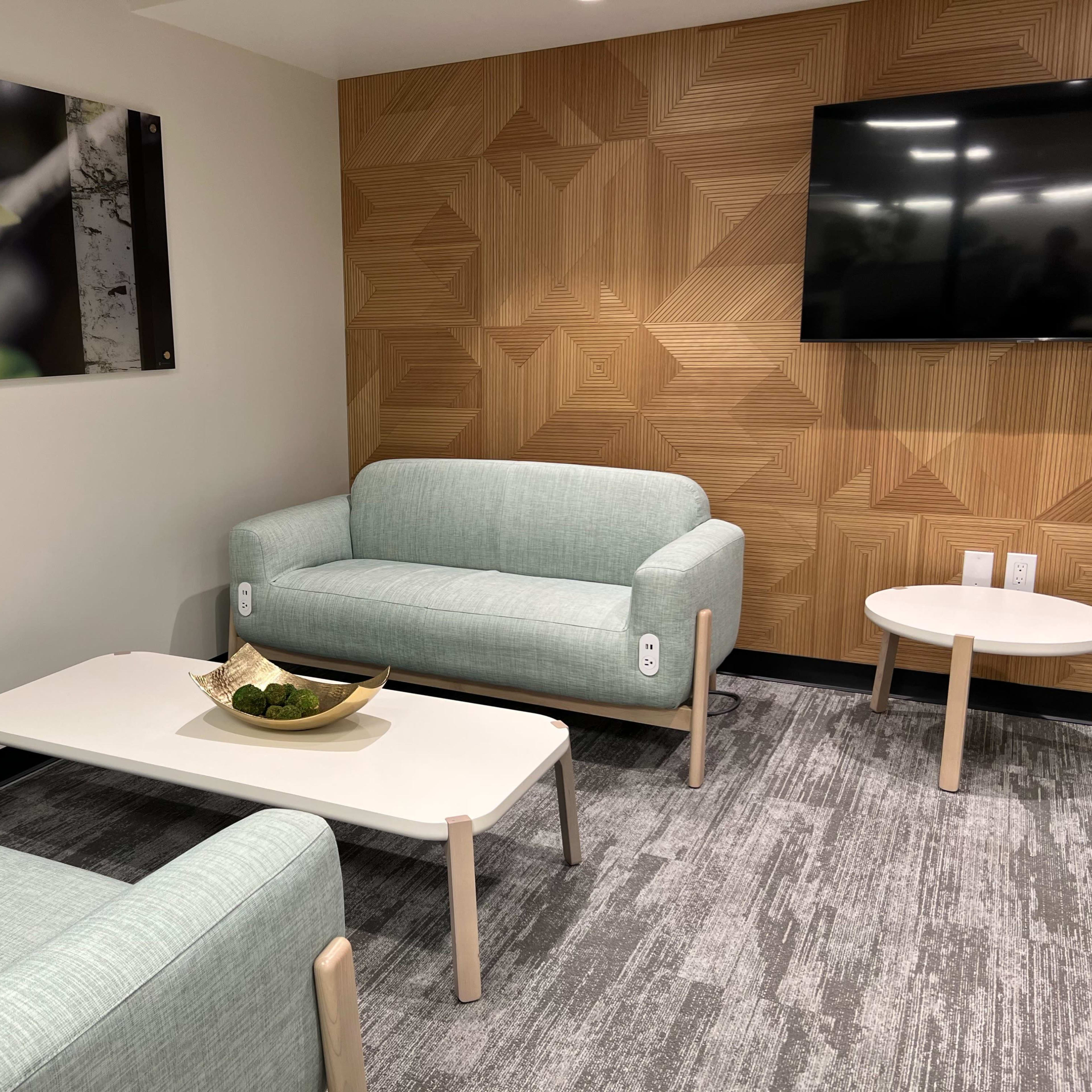 A modern lounge area with two light blue sofas, a white coffee table, and a wall-mounted flat-screen TV, featuring a textured wood panel backdrop.