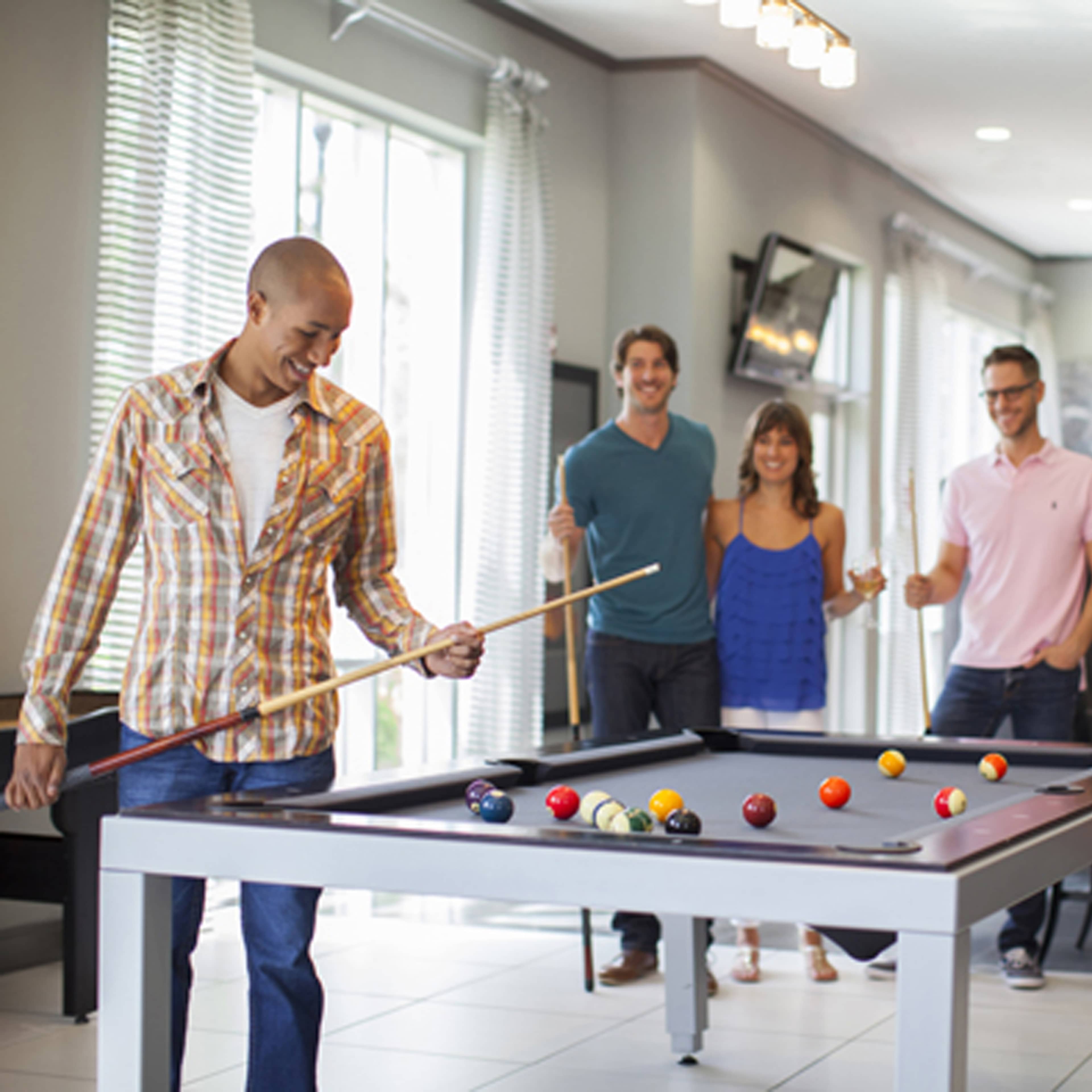 A group of four people socialize in a recreational area while one person prepares to take a shot at a pool table.