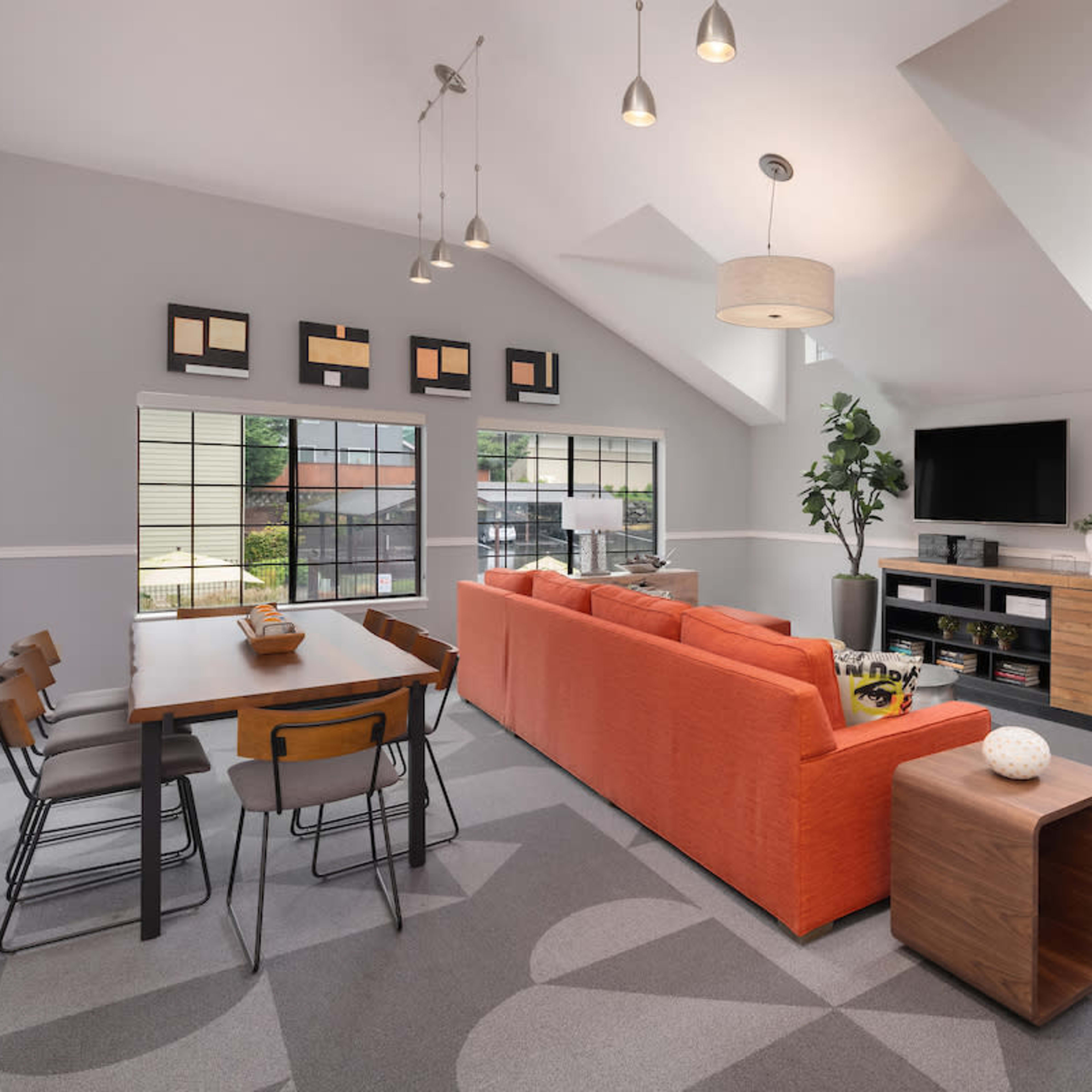 A modern living space featuring a bright orange sofa, a wooden dining table with black chairs, and a television mounted on the wall.