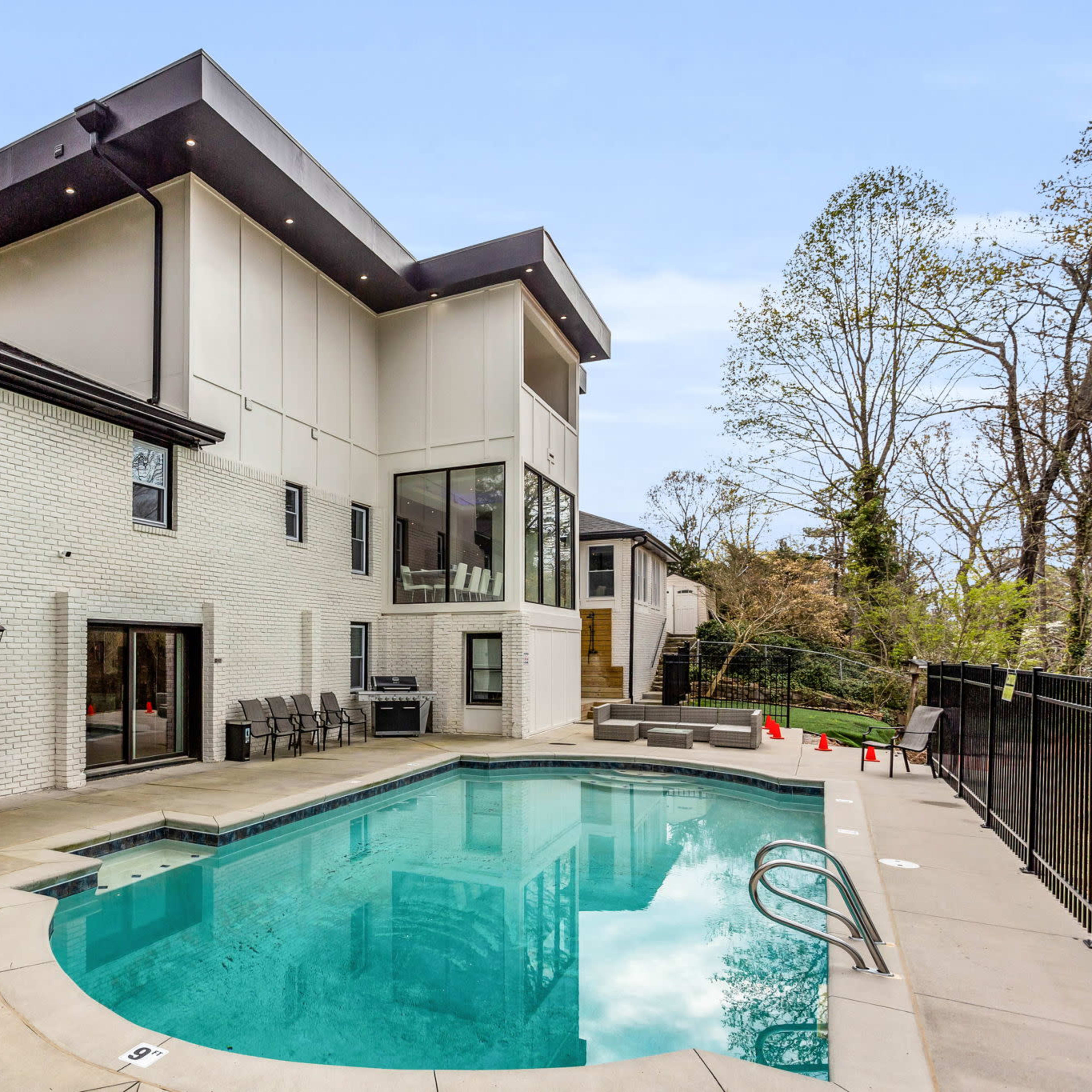 A modern home with a rectangular swimming pool, surrounded by a concrete patio and a fenced yard.