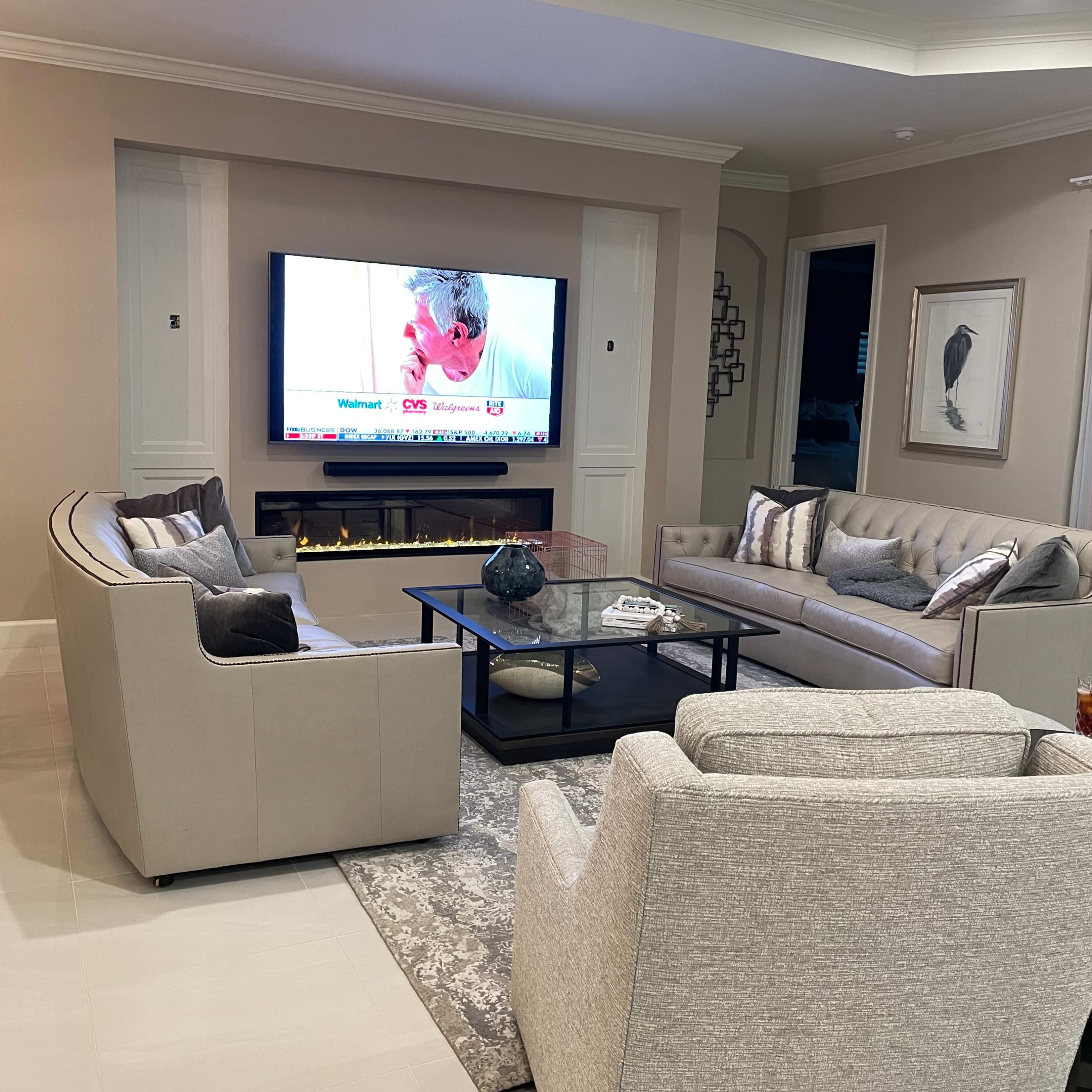 A modern living room with a television mounted on the wall, two light-colored sofas, and a coffee table on a patterned rug.