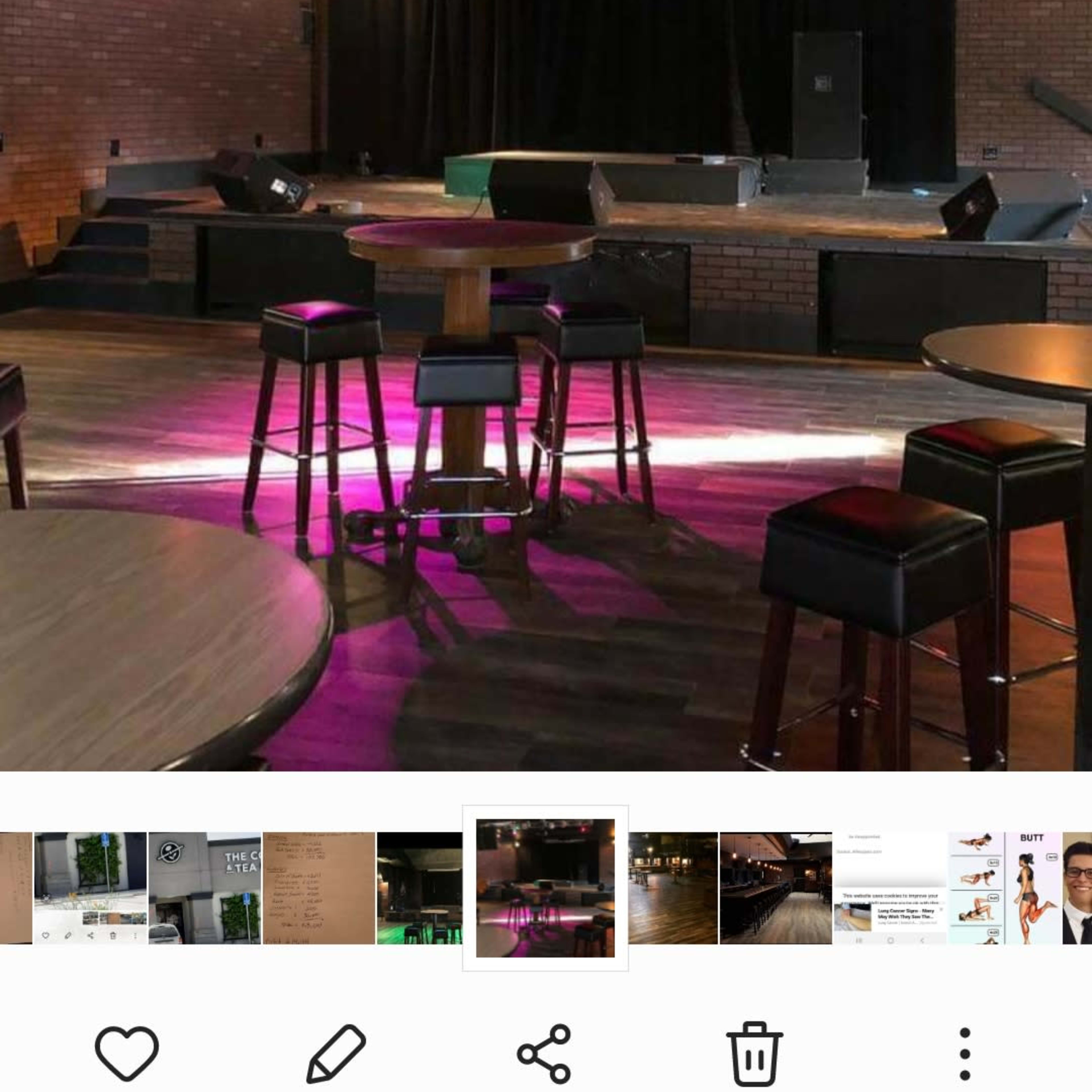 A dimly lit music venue featuring a stage with lights, surrounded by empty tables and stools.