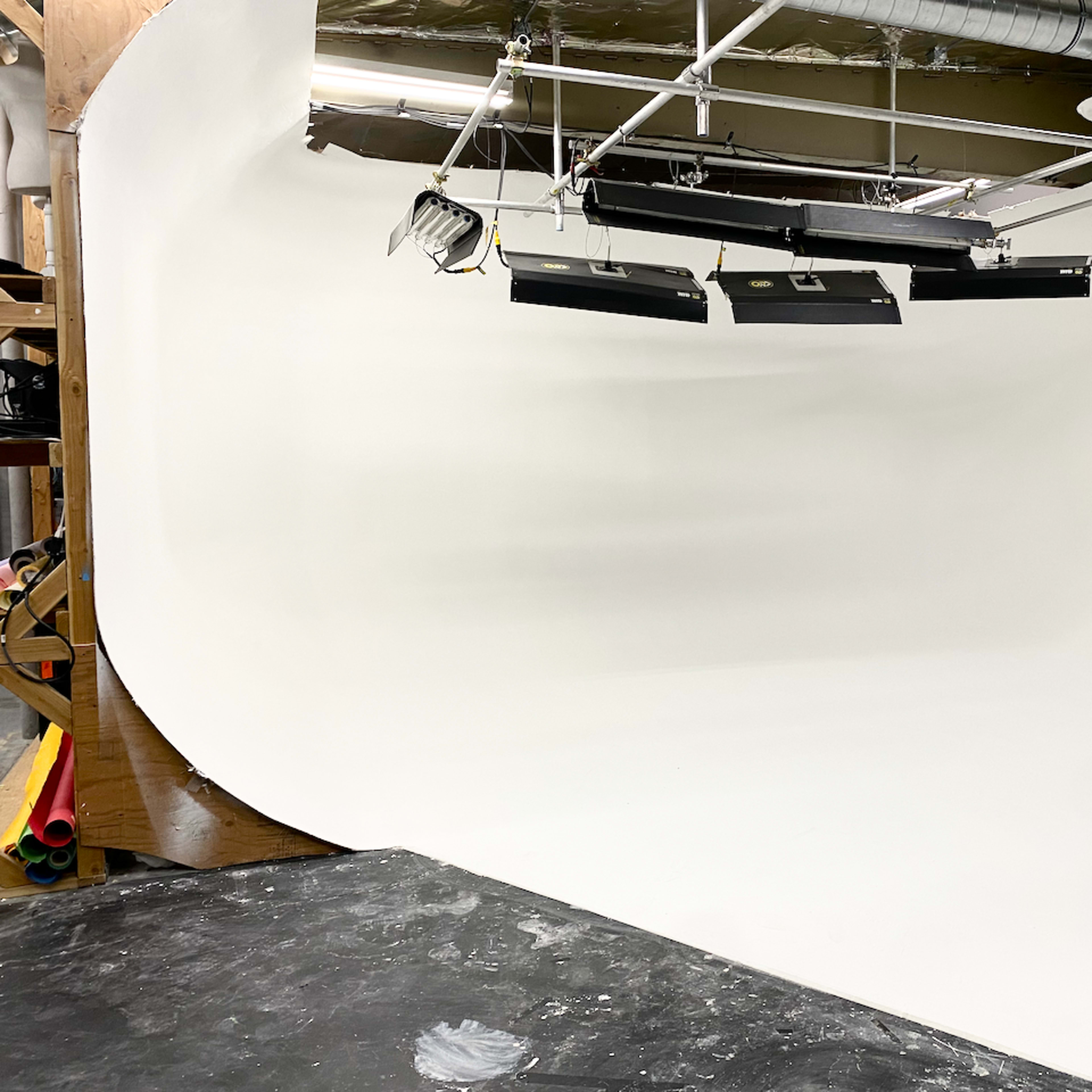 A photography studio with a curved white backdrop and studio lights suspended from the ceiling.