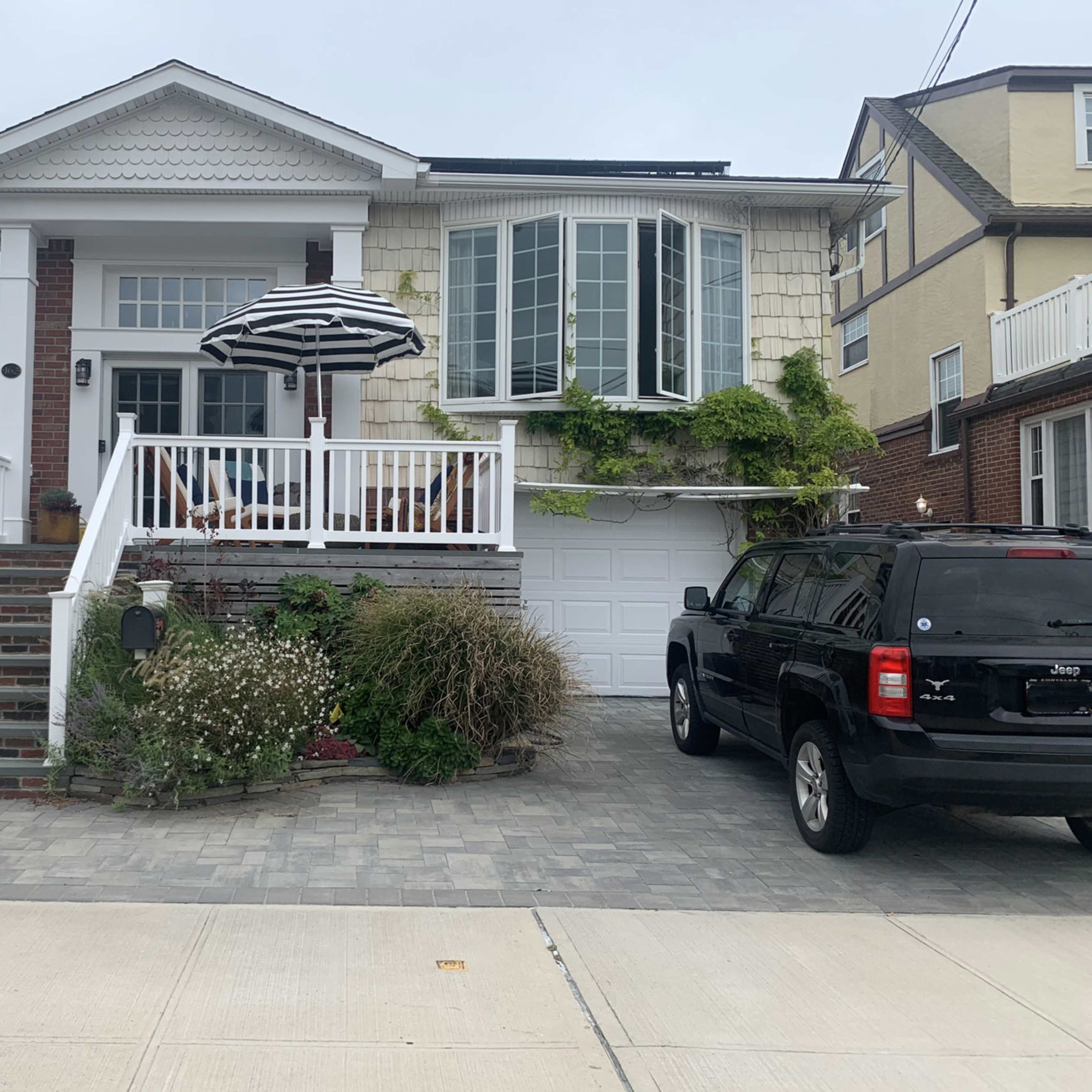 A two-story house with a front porch, an umbrella, and a landscaped yard, along with a driveway containing a black SUV.