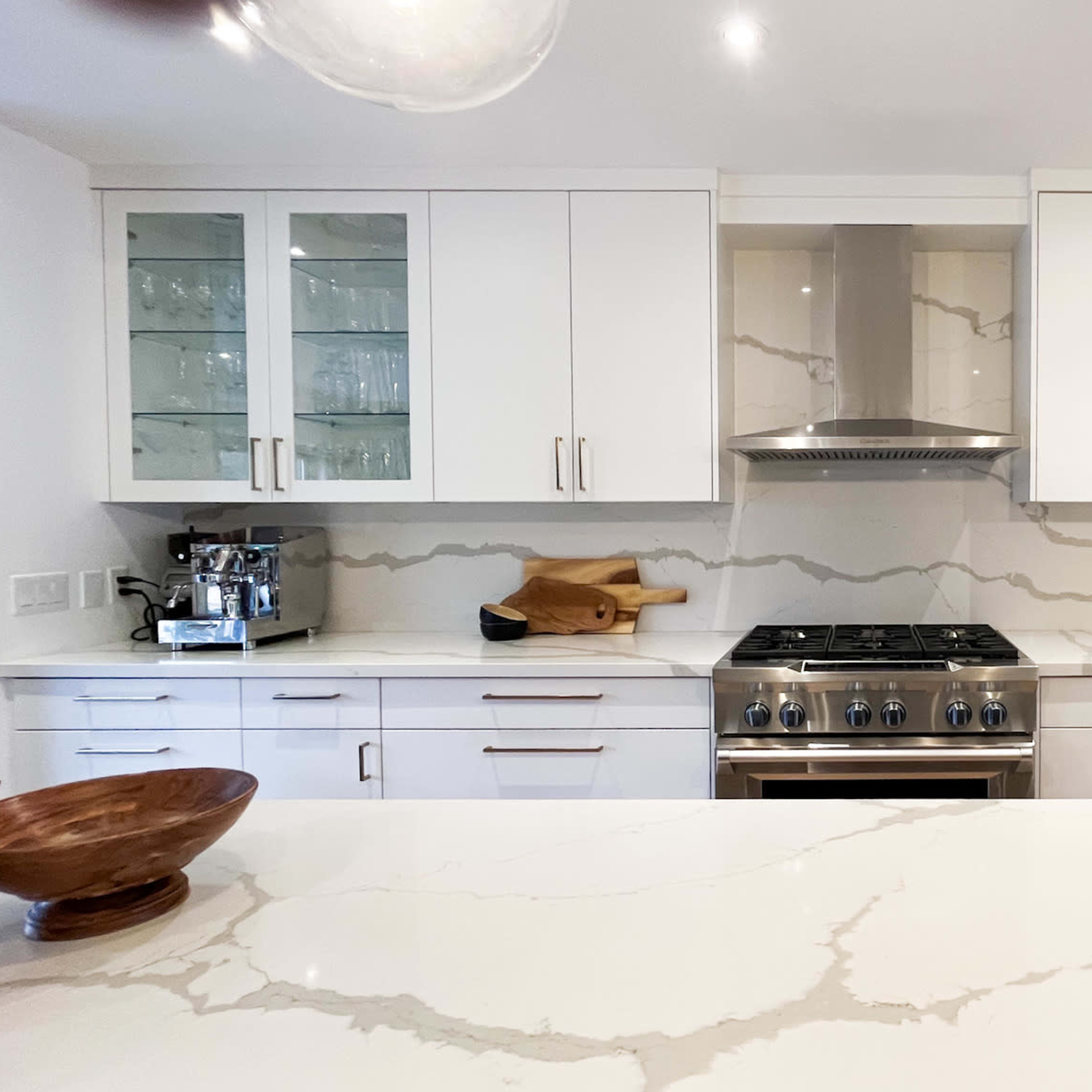 The kitchen features white cabinetry, a stainless steel stove with an overhead vent, and a marble backsplash.