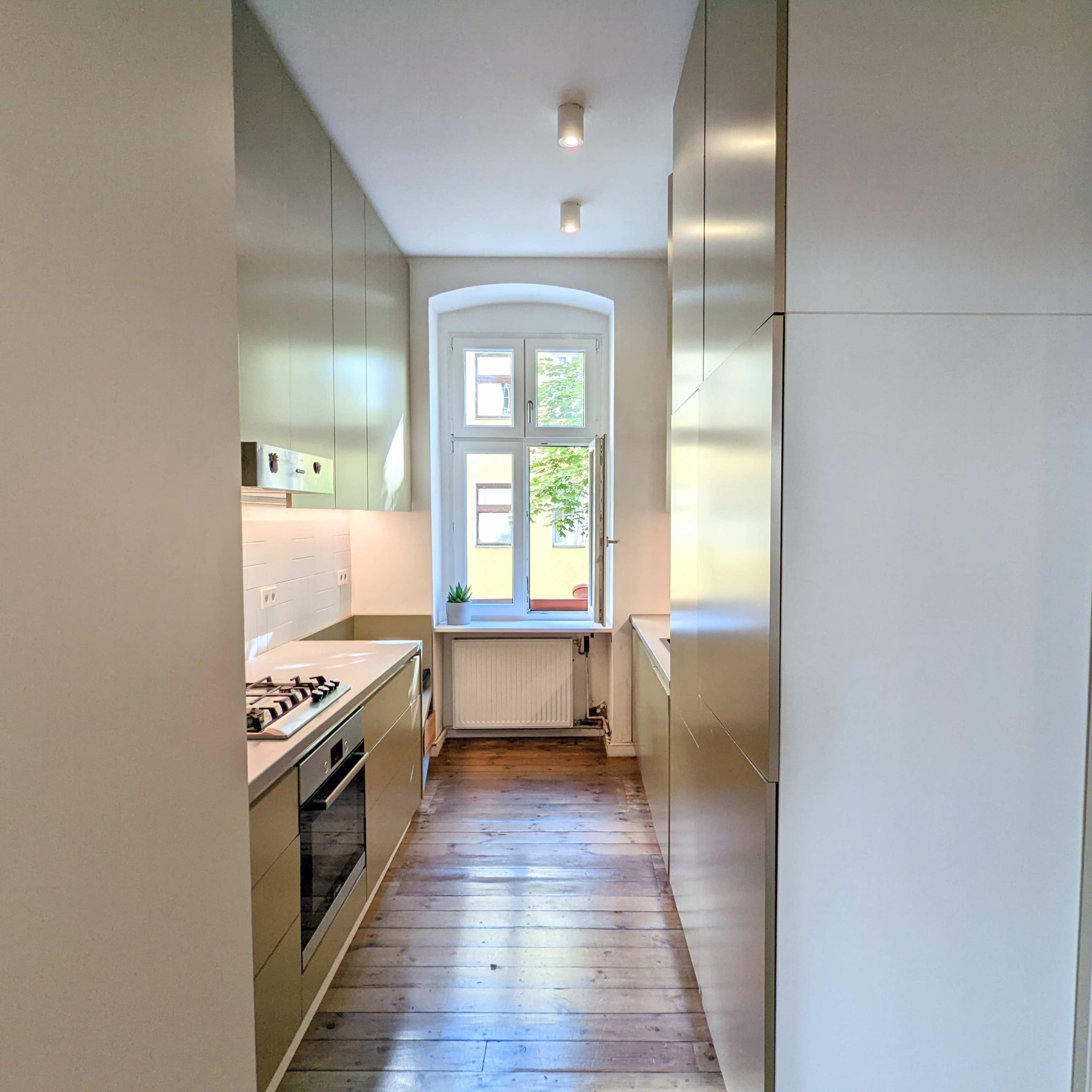 A narrow kitchen featuring modern cabinetry, a gas stove, and a window that allows natural light to enter.