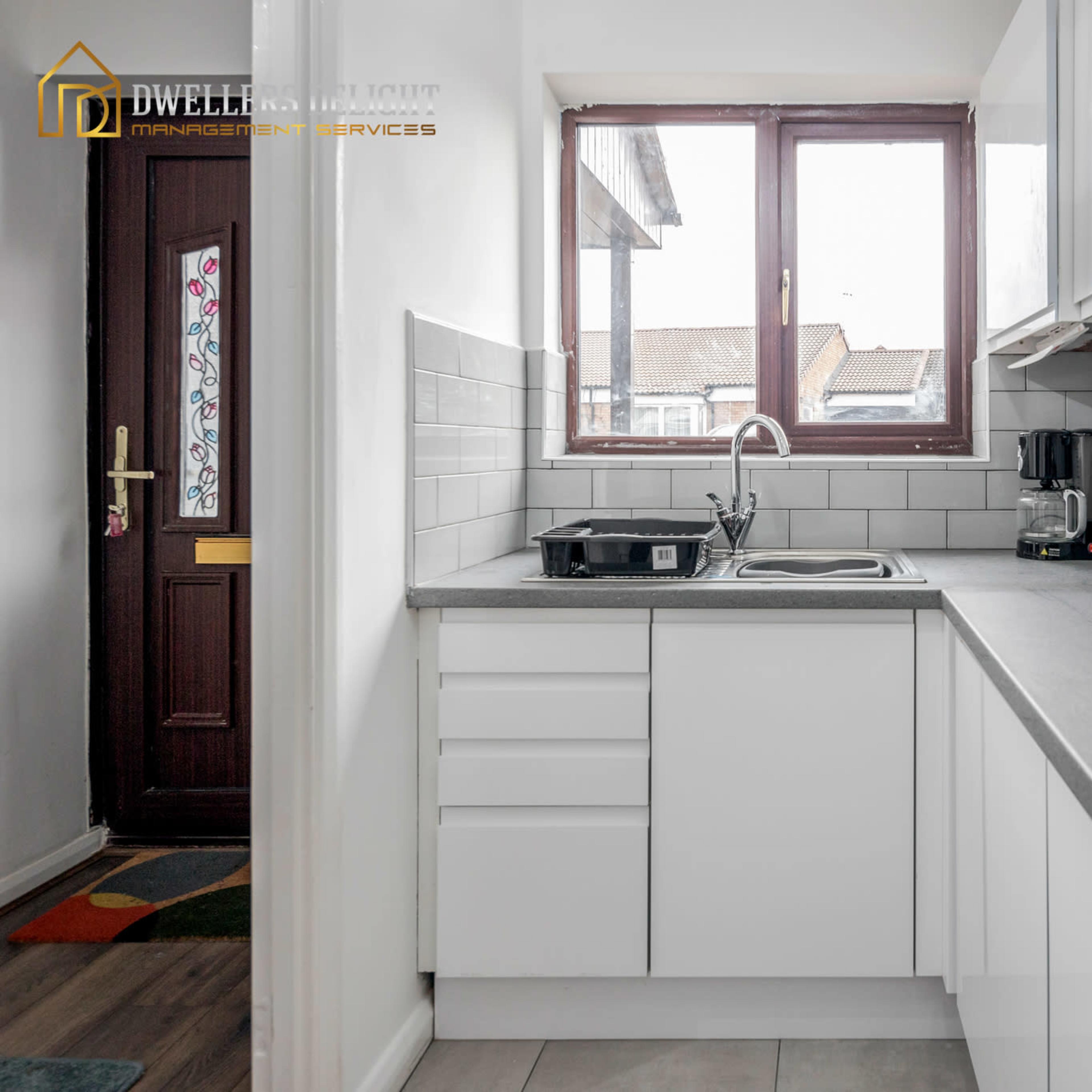 A modern kitchen with white cabinets, a gray countertop, and a window above the sink.