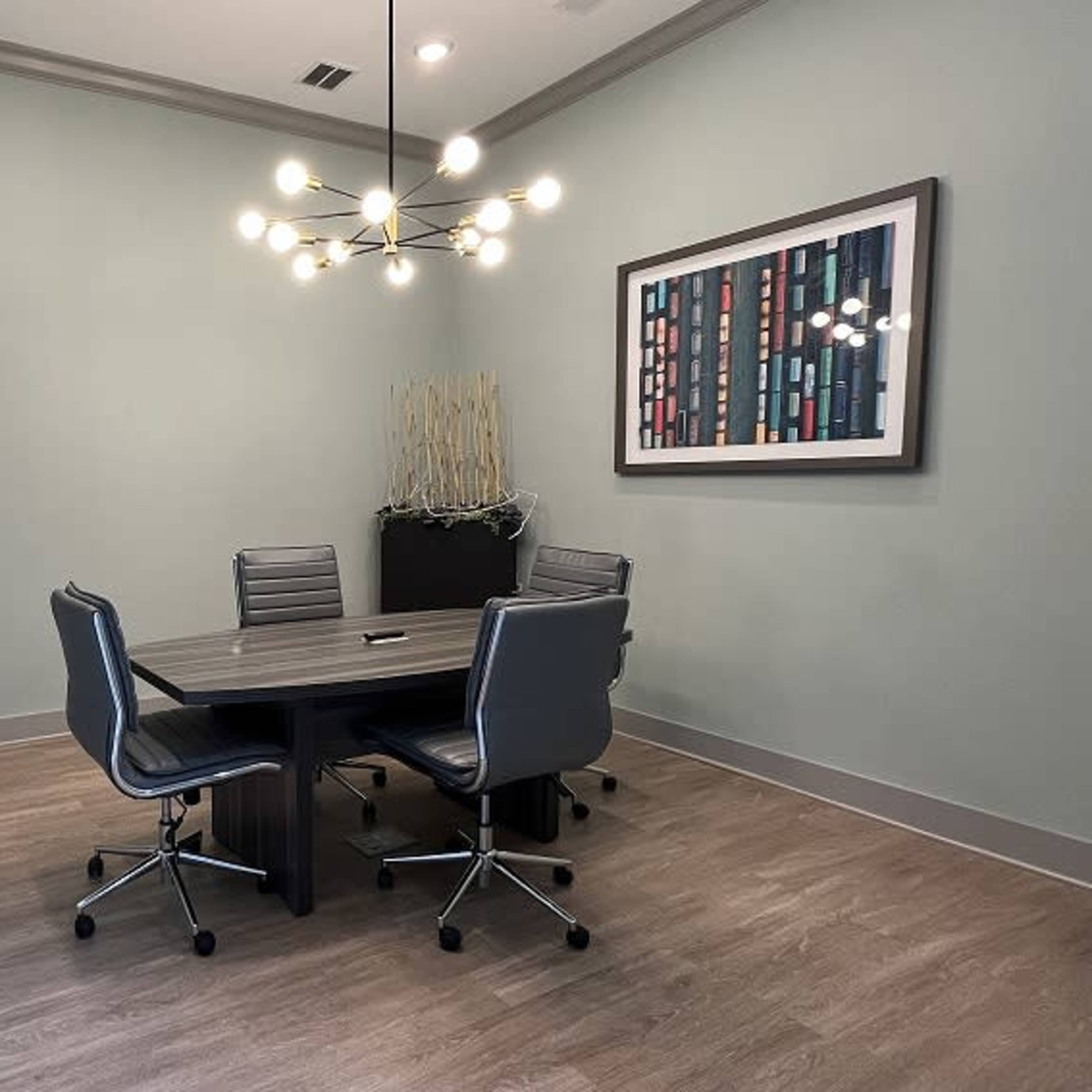 A small conference room features a round table surrounded by four chairs, a wall-mounted TV, and decorative plants.