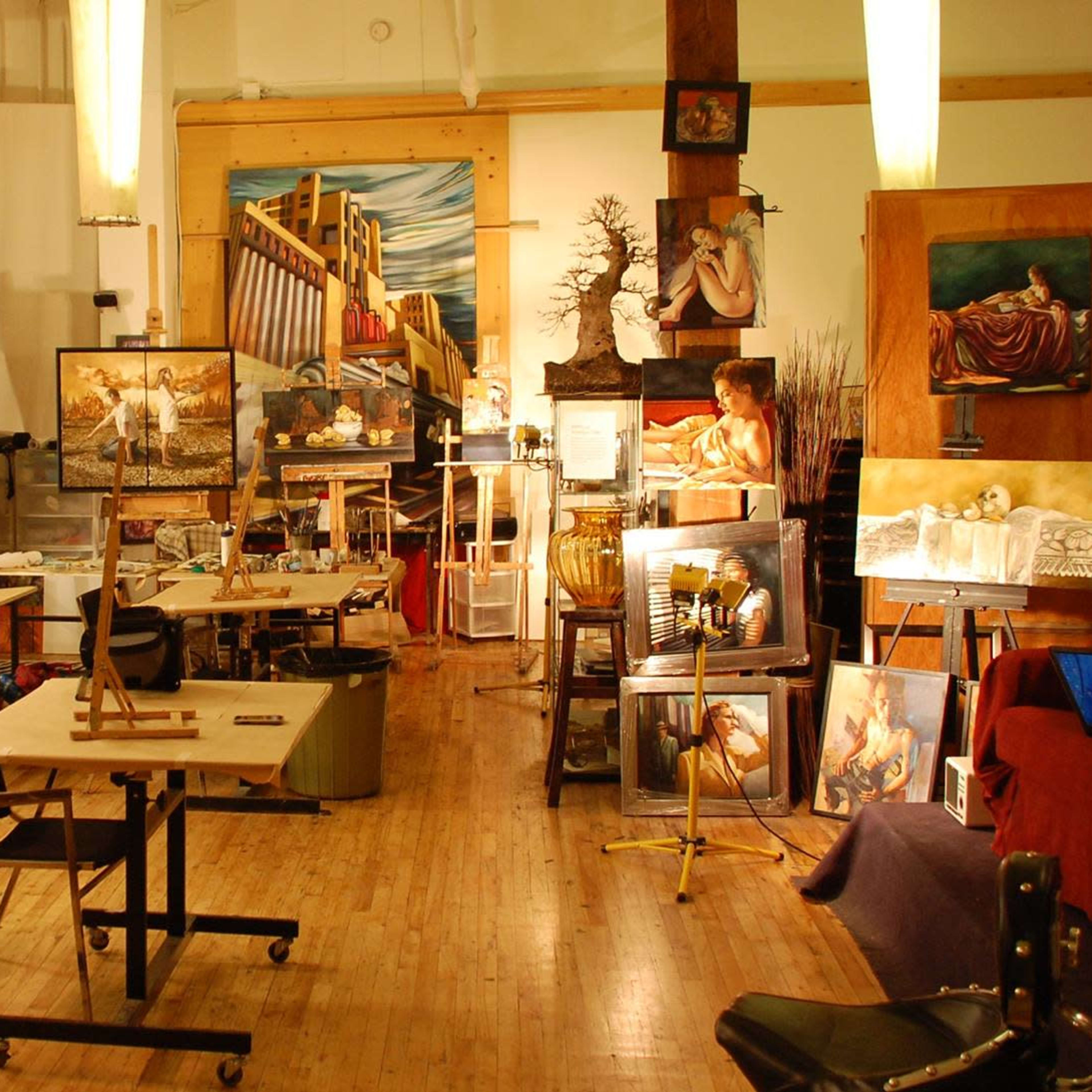 An art studio filled with easels, tables, and various paintings displayed around the room.
