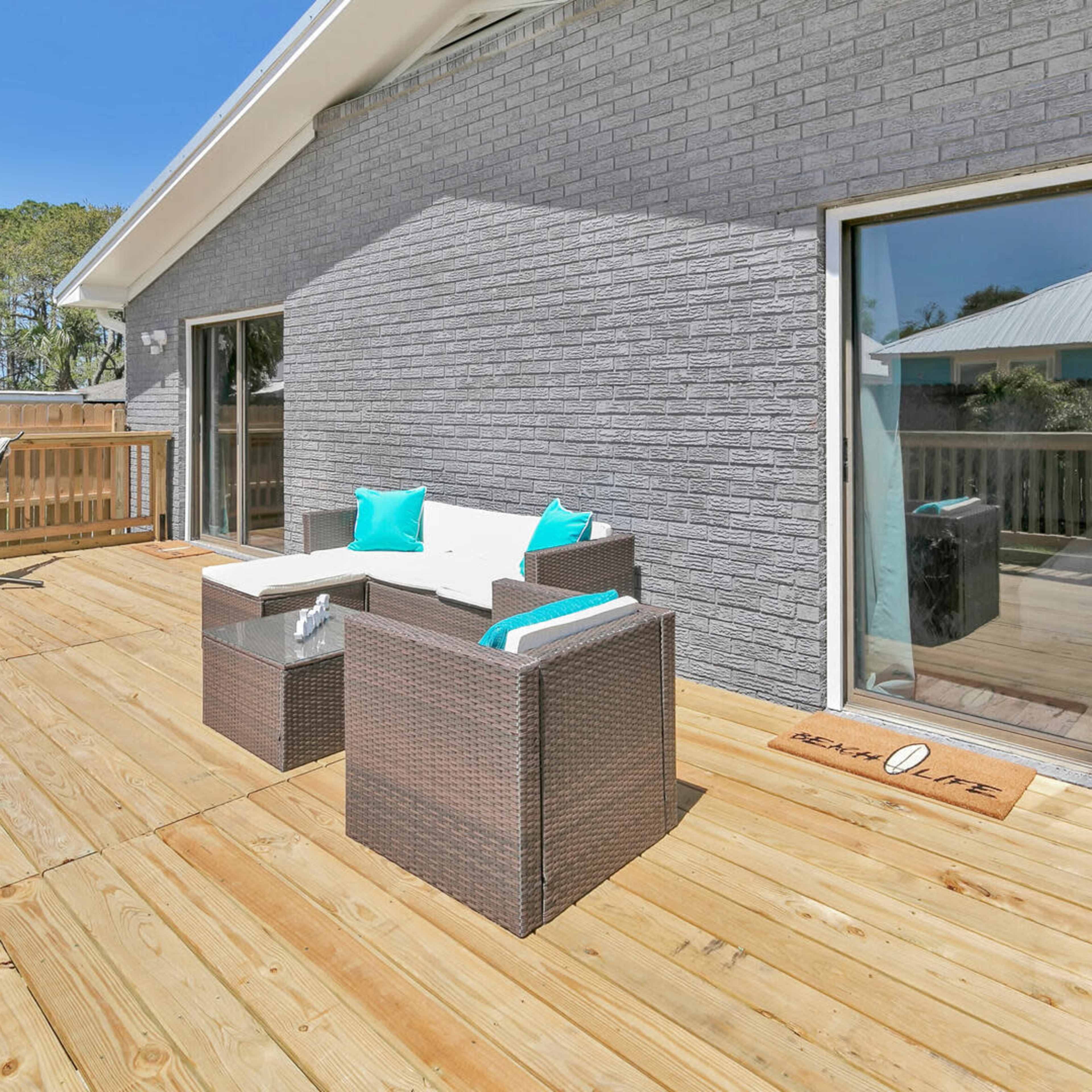 A wooden deck with modern outdoor seating, a hammock, and sliding glass doors leading to an interior space.
