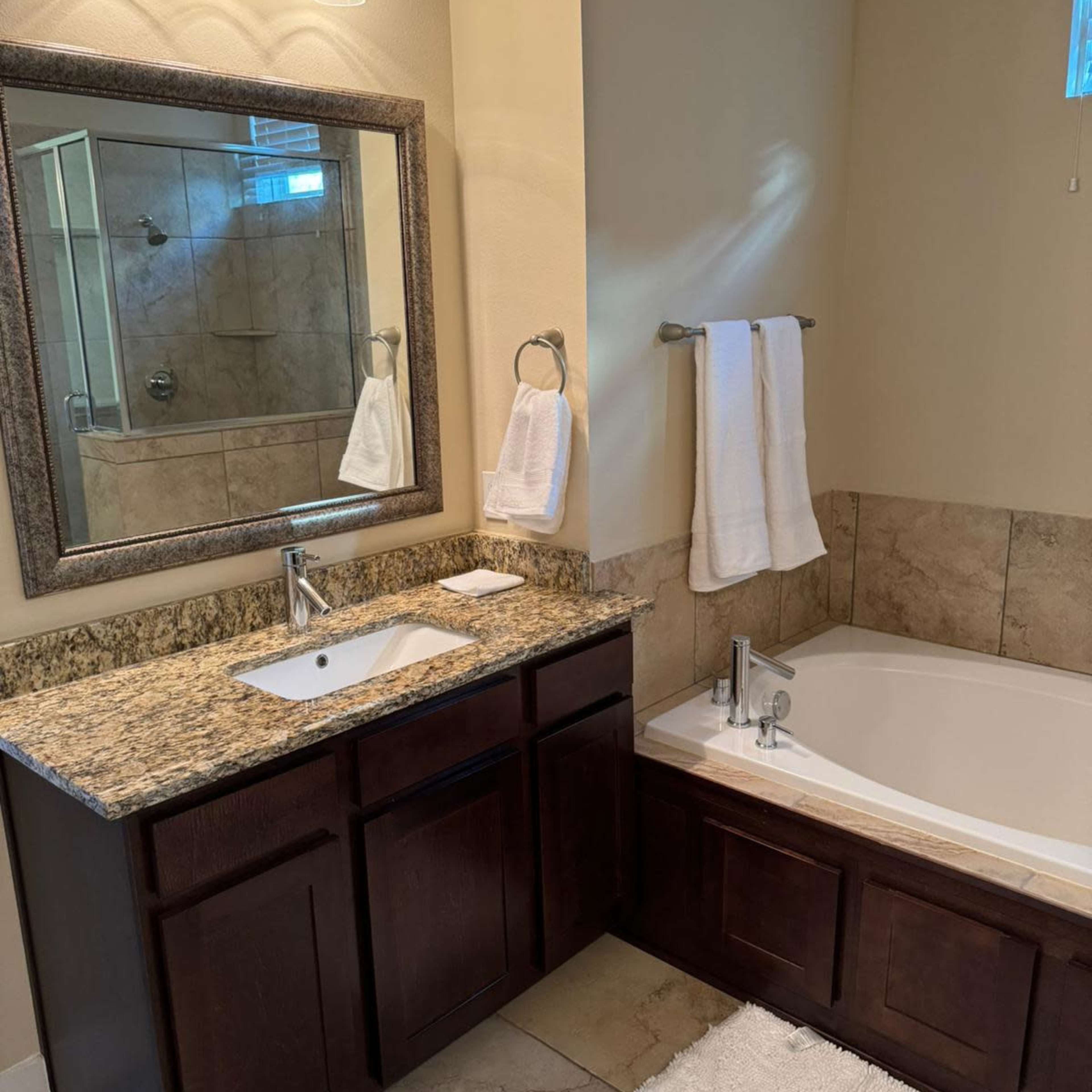 A bathroom features a double vanity with a granite countertop, a large mirror, and a separate soaking tub next to a glass-enclosed shower.
