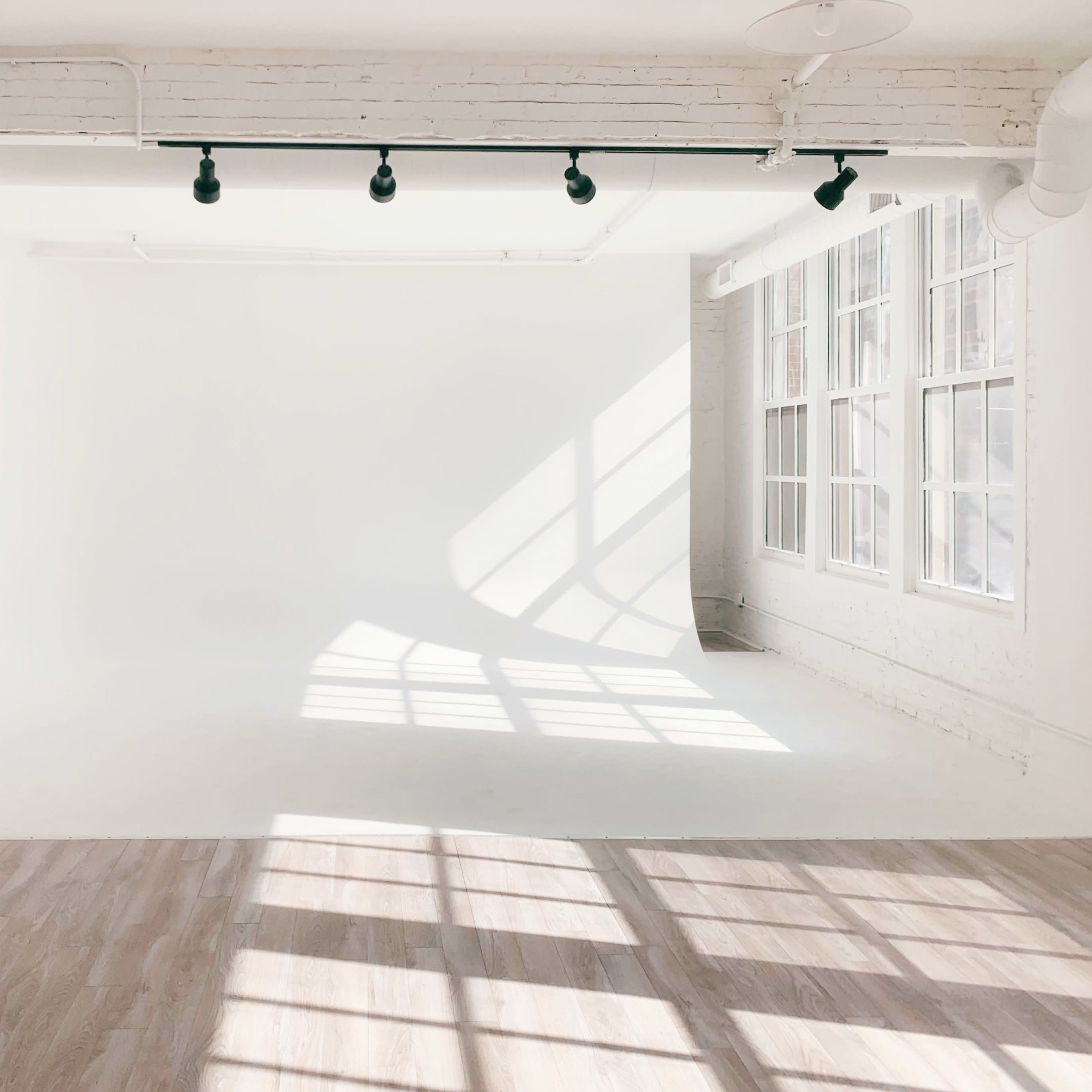 A bright, empty studio space with large windows and gentle shadows on the floor.