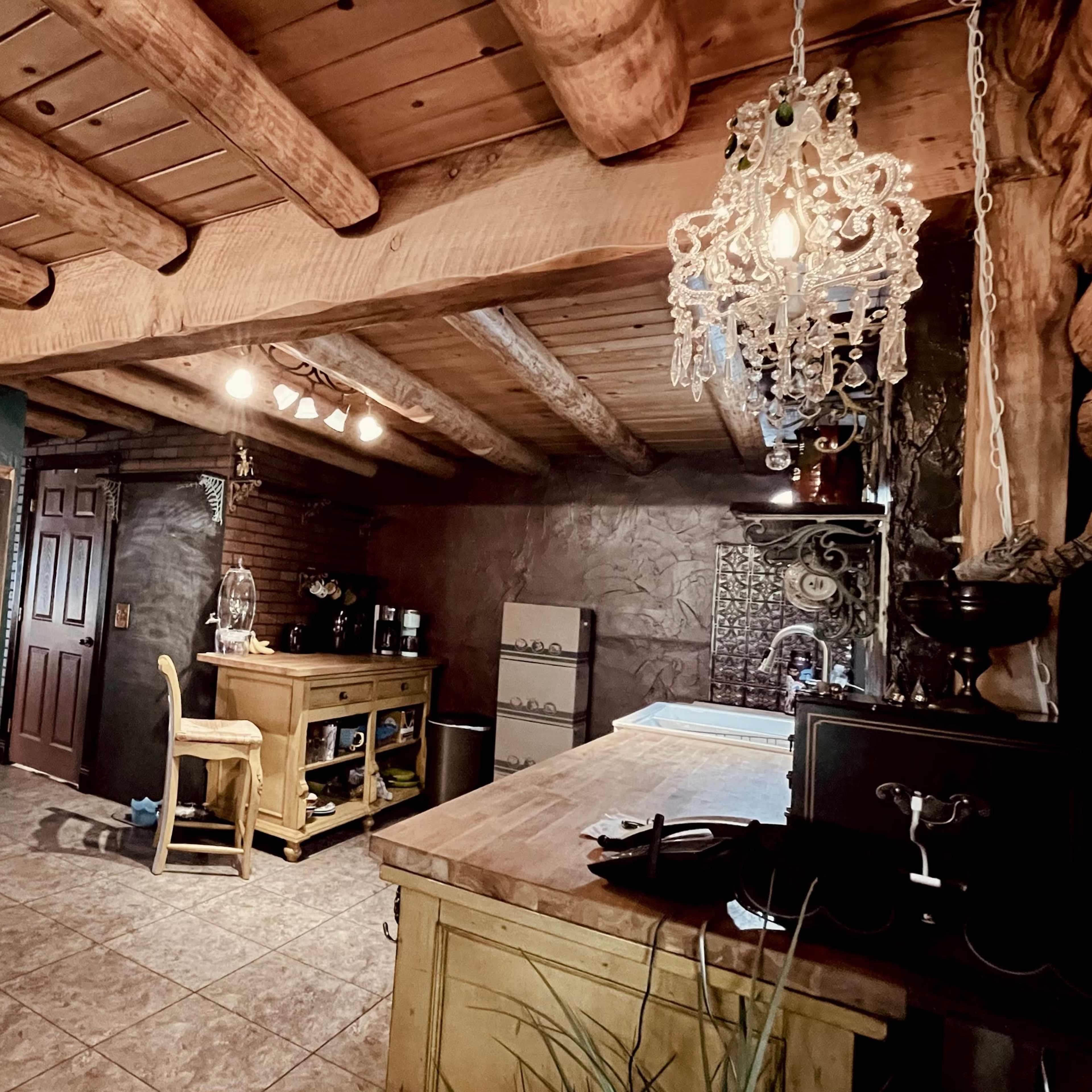 A rustic kitchen featuring log beams, wooden cabinetry, a stainless steel refrigerator, and a chandelier.