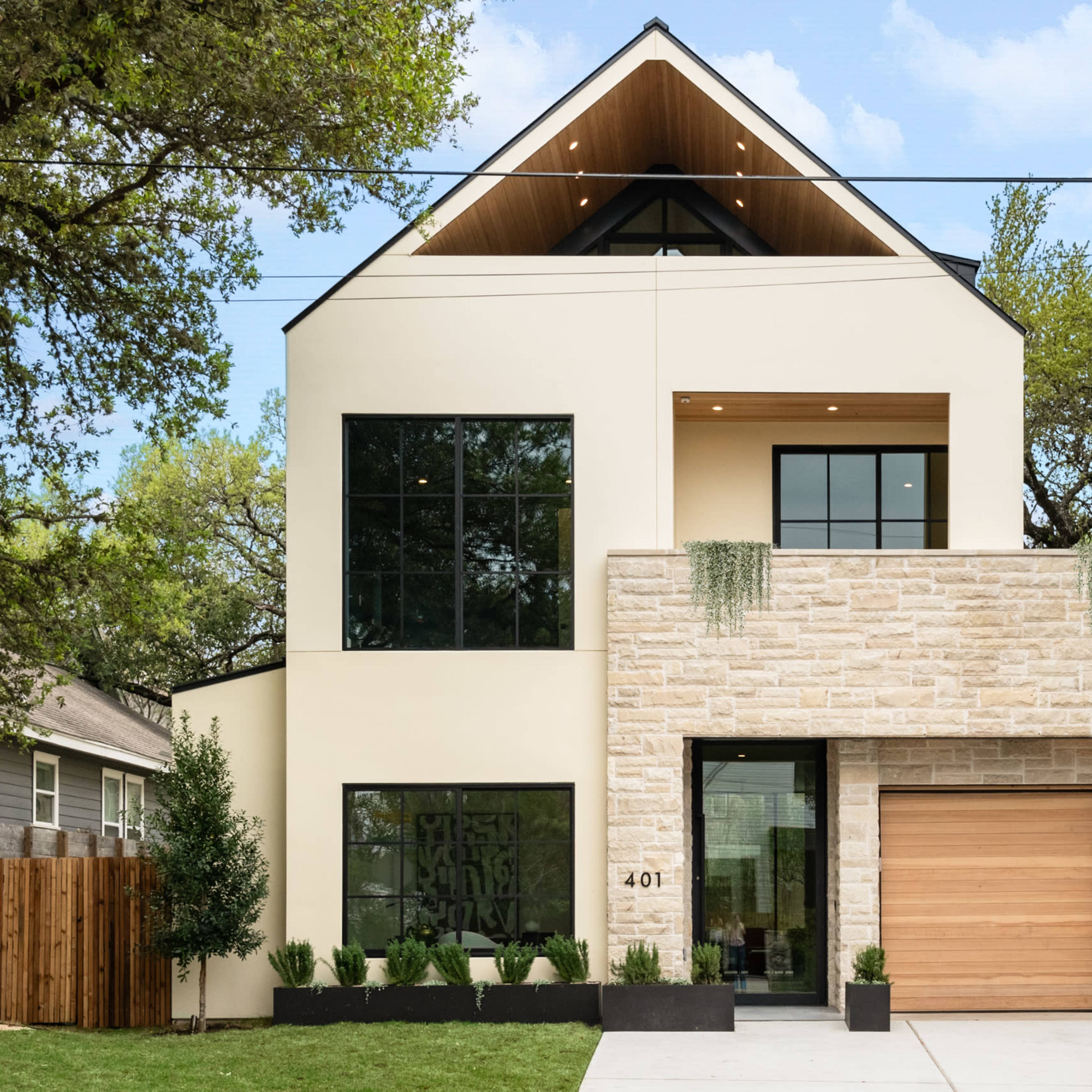 A modern two-story house with a stone and cream-colored exterior, large windows, and a wooden garage door.