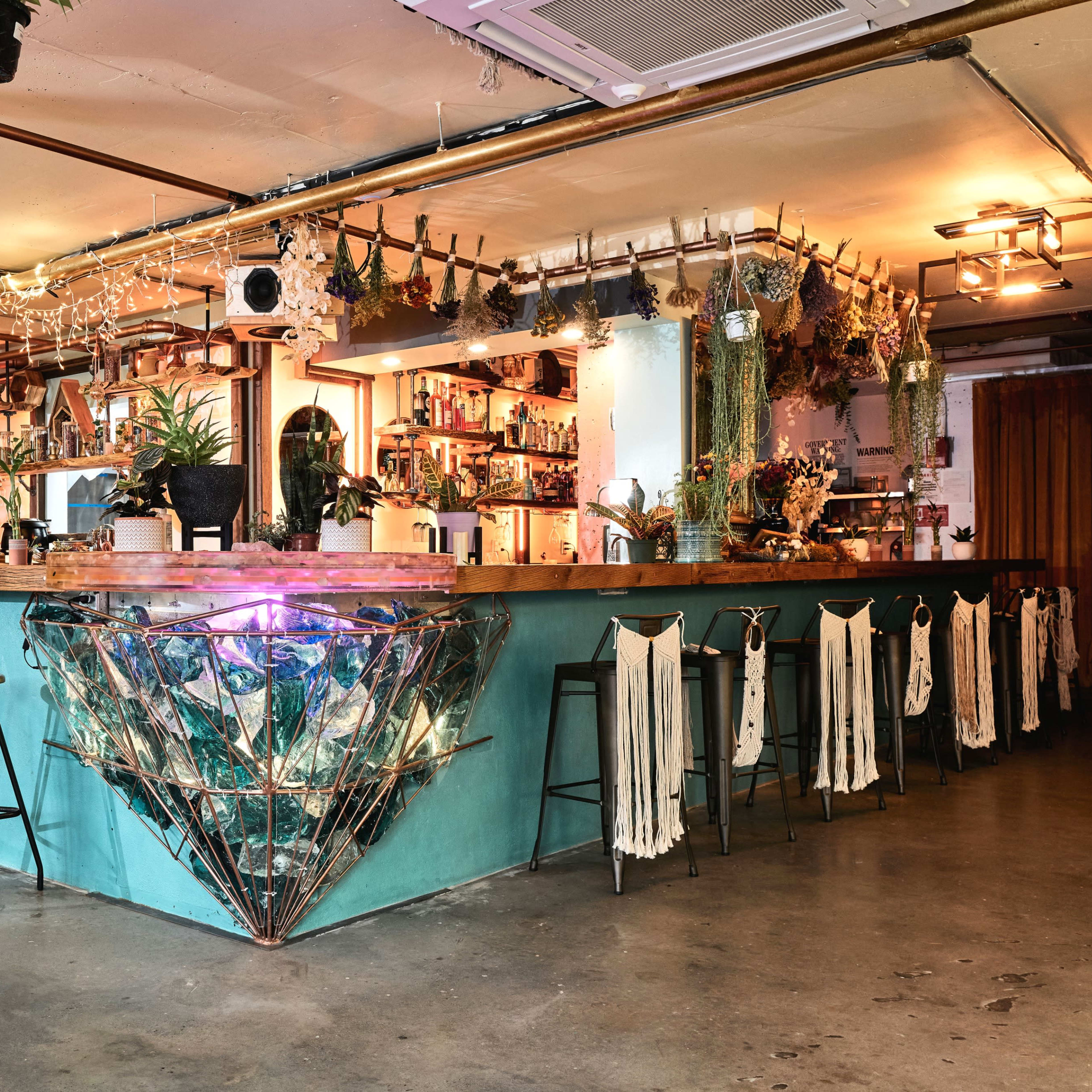 A bar area with a unique diamond-shaped counter, surrounded by high stools, and decorated with plants and colorful lighting.