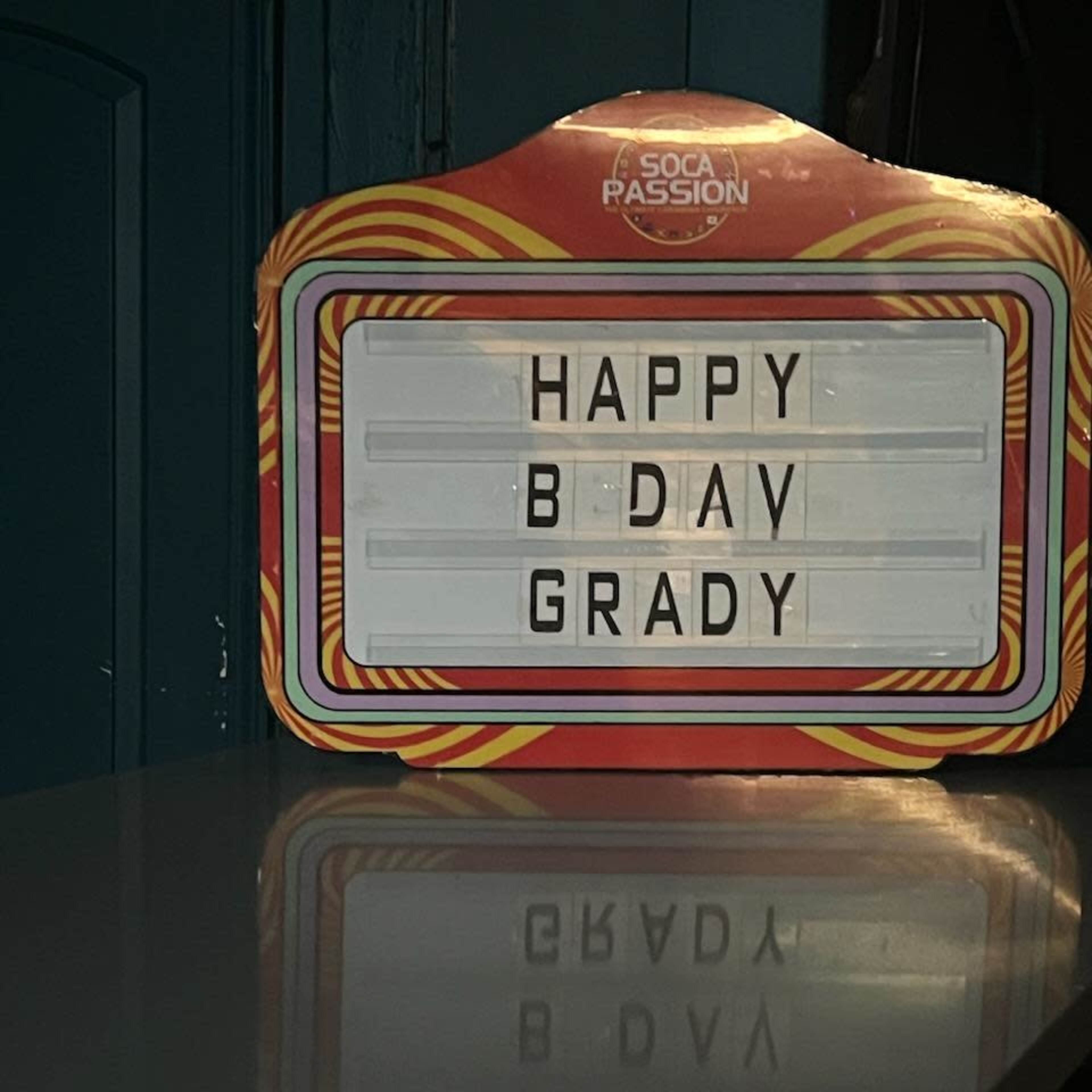A lit sign on a table reads "HAPPY B DAV GRADY."