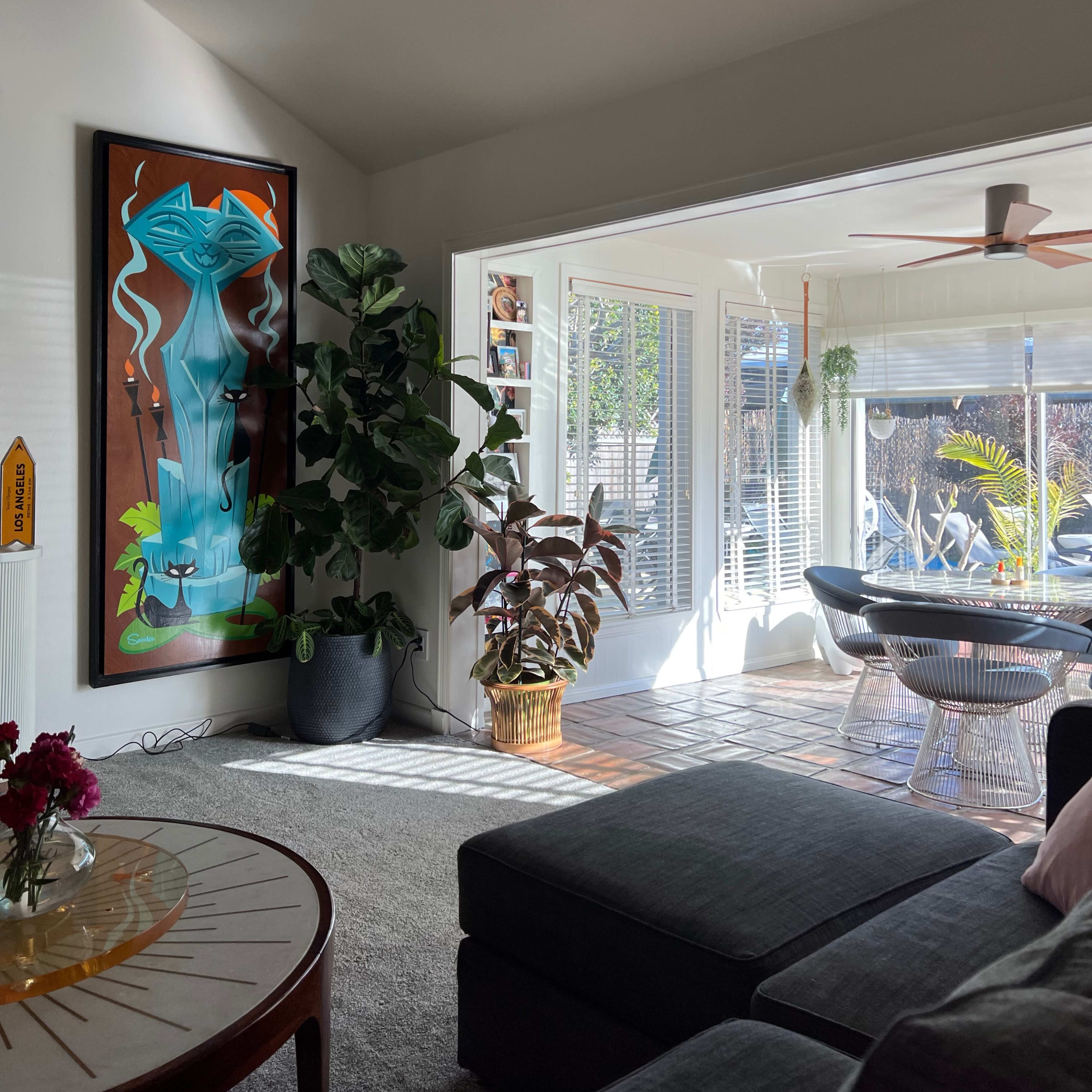 A bright living room featuring a large colorful artwork, a potted plant, and an open area leading to a sunlit patio.